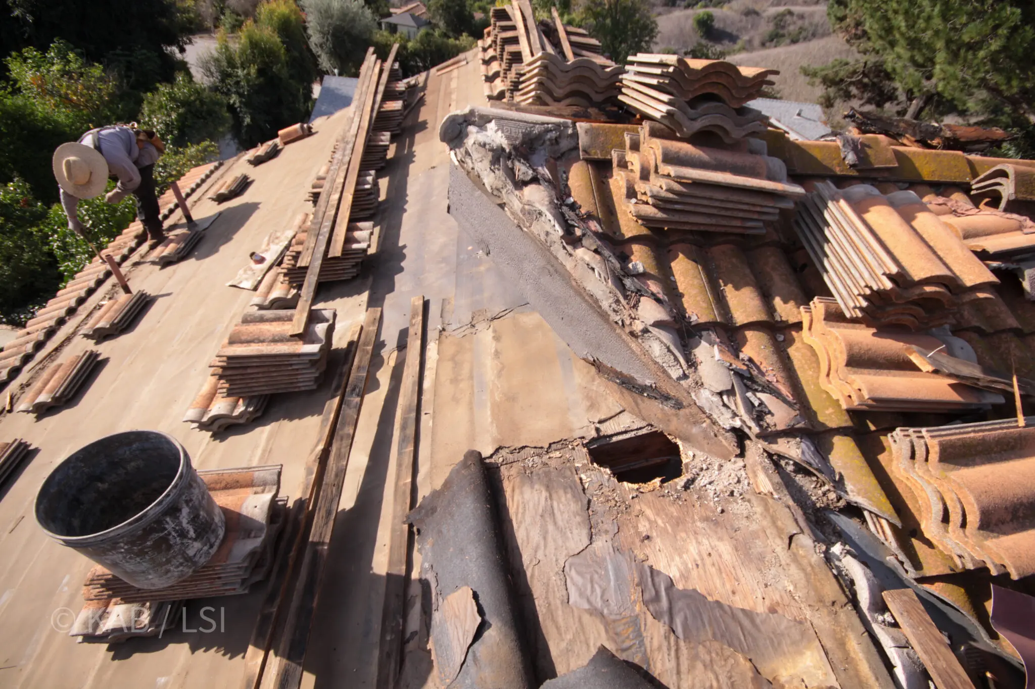 Concrete roof tile lifted and stacked to reveal cooked underlayment and rotted sheathing beneath, on a hillside home in La Habra Heights
