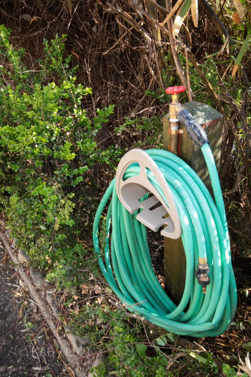 Outdoor hose bib on a wooden post with a coiled garden hose, part of a hillside property water station