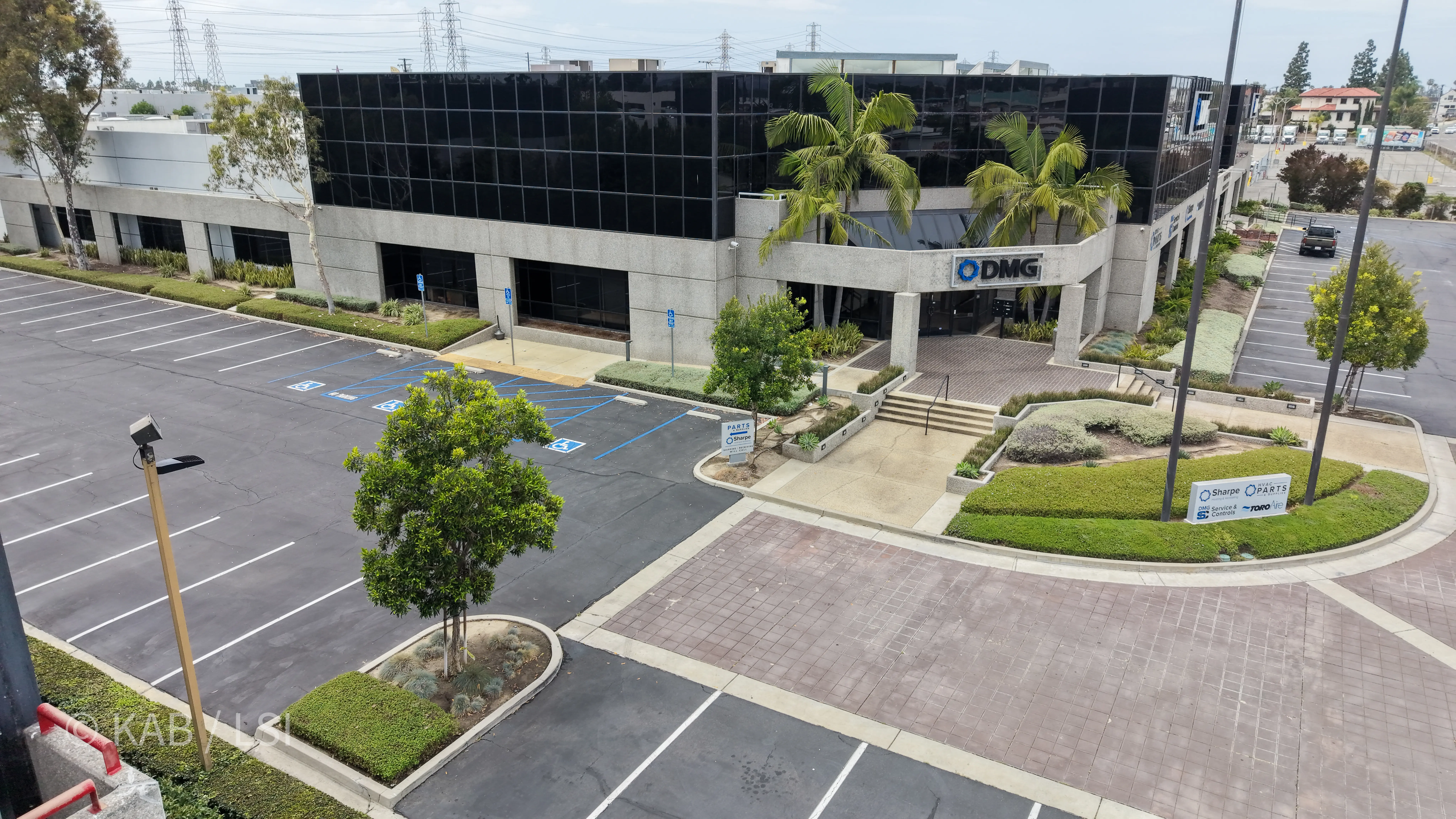 Front entry of the 88,000 sq ft commercial building at 1110 W. Taft Ave., Orange, CA, with DMG HVAC signage above the portico, queen palms, brick paver walkway, and tenant directory monument visible.