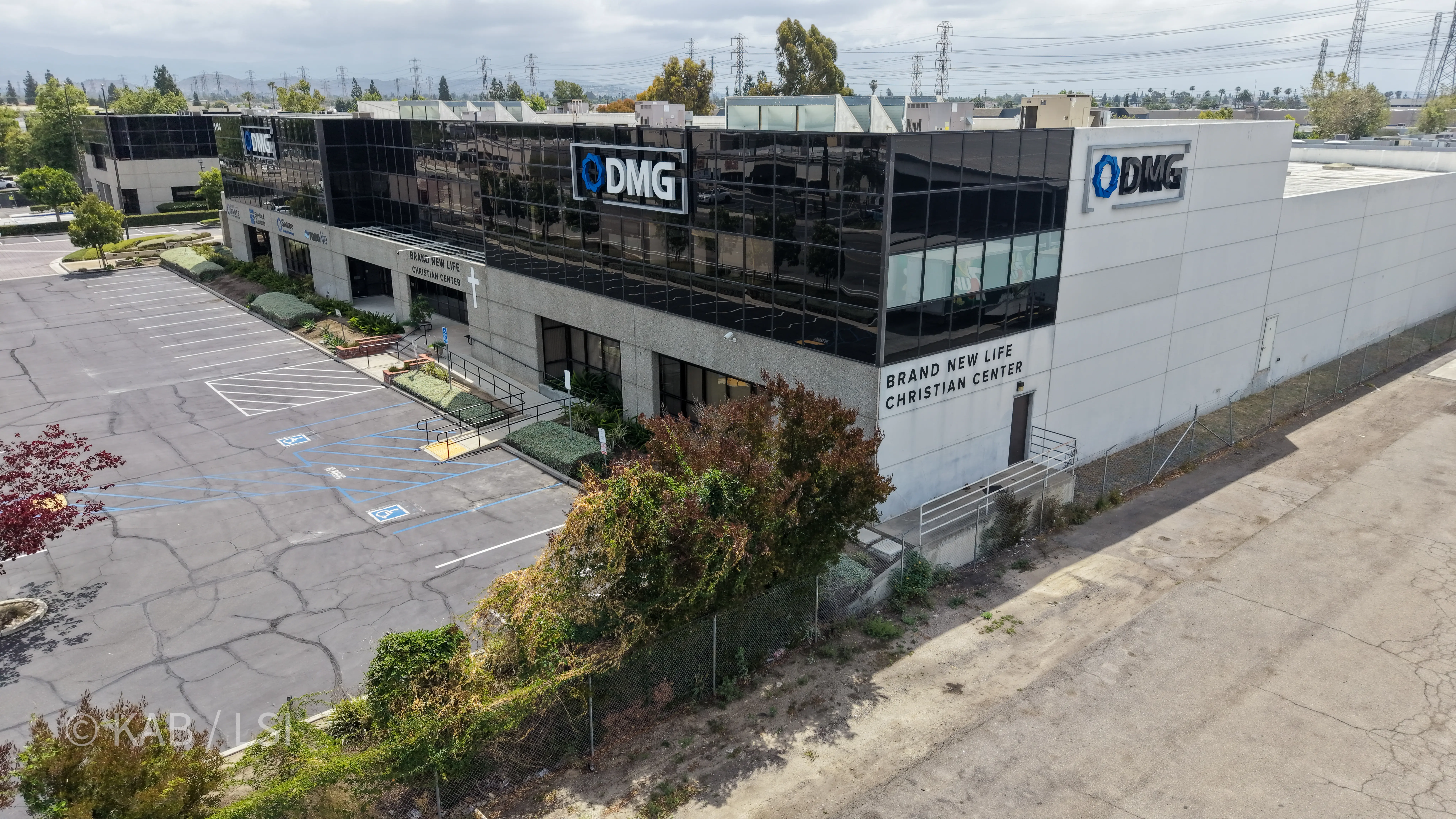 Aerial side view of the 88,000 sq ft building at 1110 W. Taft Ave., Orange, CA, showing DMG HVAC signage and Brand New Life Christian Center signage on the side wall, with the Saddleback foothills in the distance.