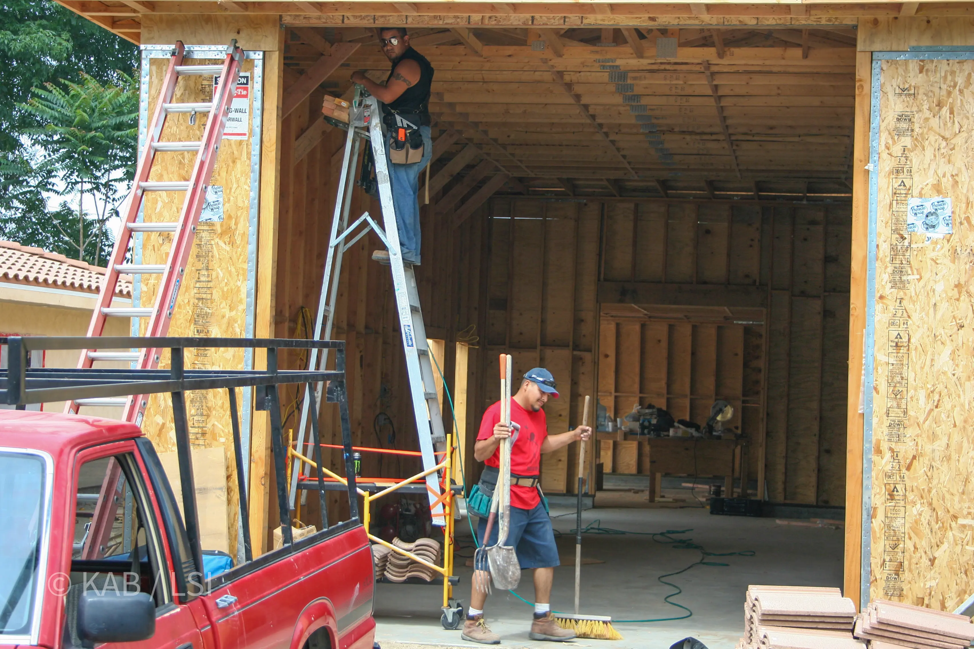 Crew at work at the RV garage entry — finish stage, ladder, sweeping the slab © KAB/LSI