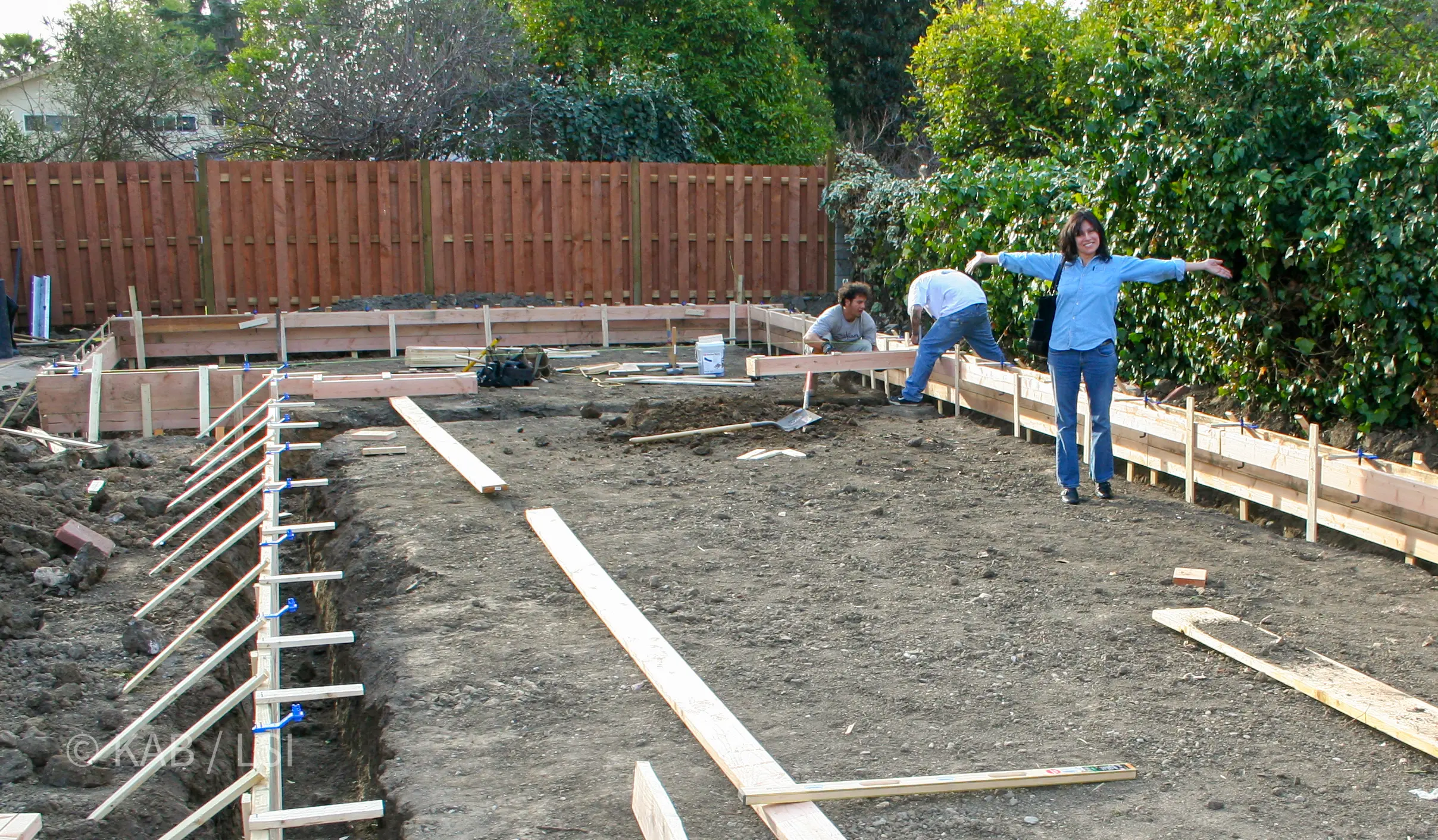 Linda standing on the first 25 feet of her 60-foot-deep RV garage-to-be — forms stage, arms wide © KAB/LSI
