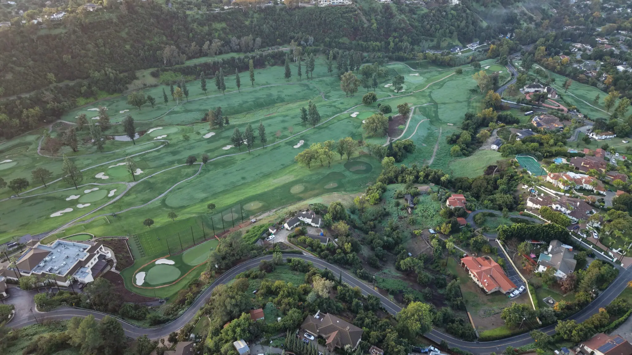 Aerial drone view of La Habra Heights at dawn, the Hacienda Golf Club fairways visible at left and hillside homes nestled into the canyon below the ridge