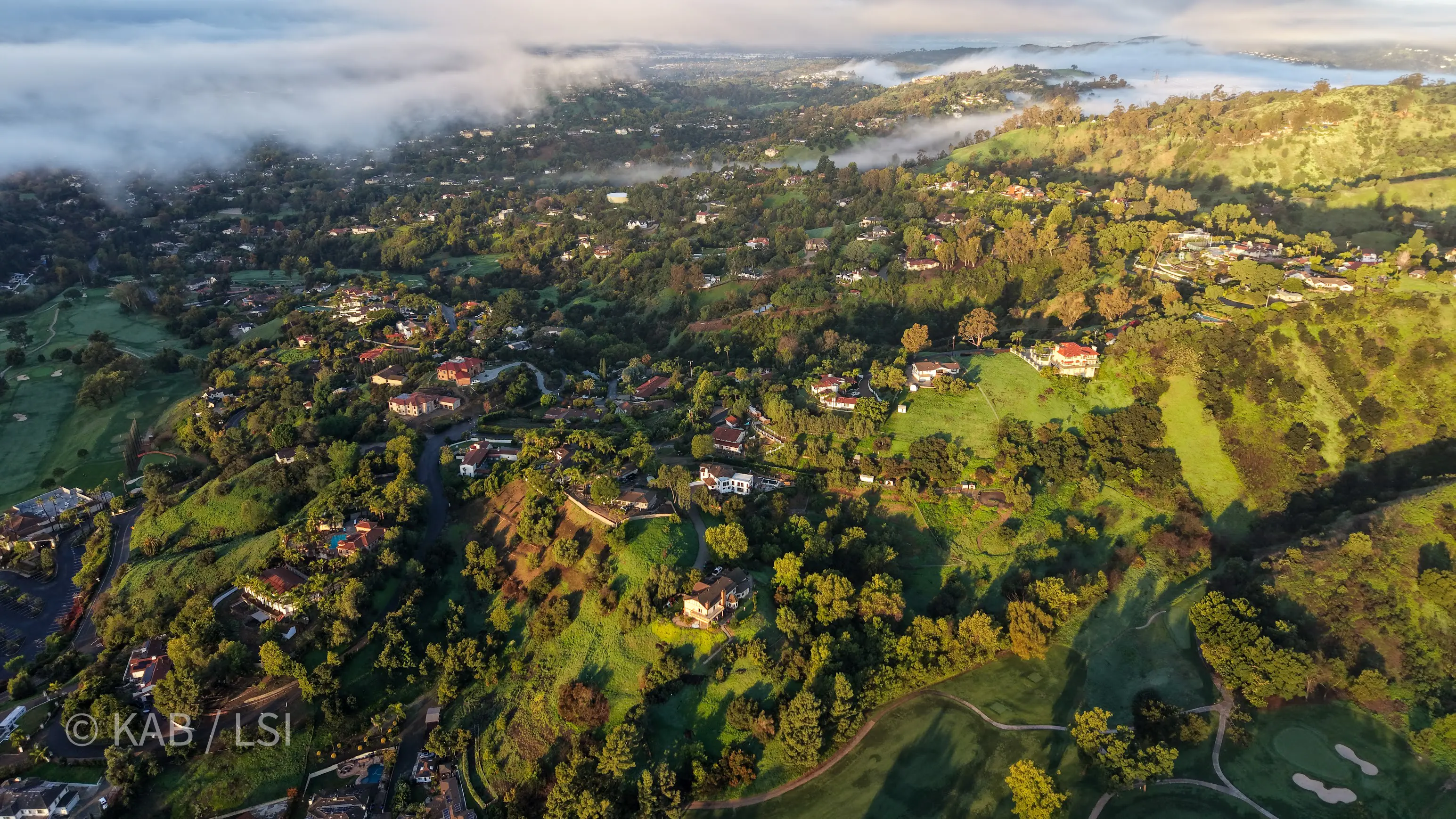 Aerial view of La Habra Heights at dawn — fog drifting through the canyon, looking north-west across the Hacienda Golf Club after a Pacific storm