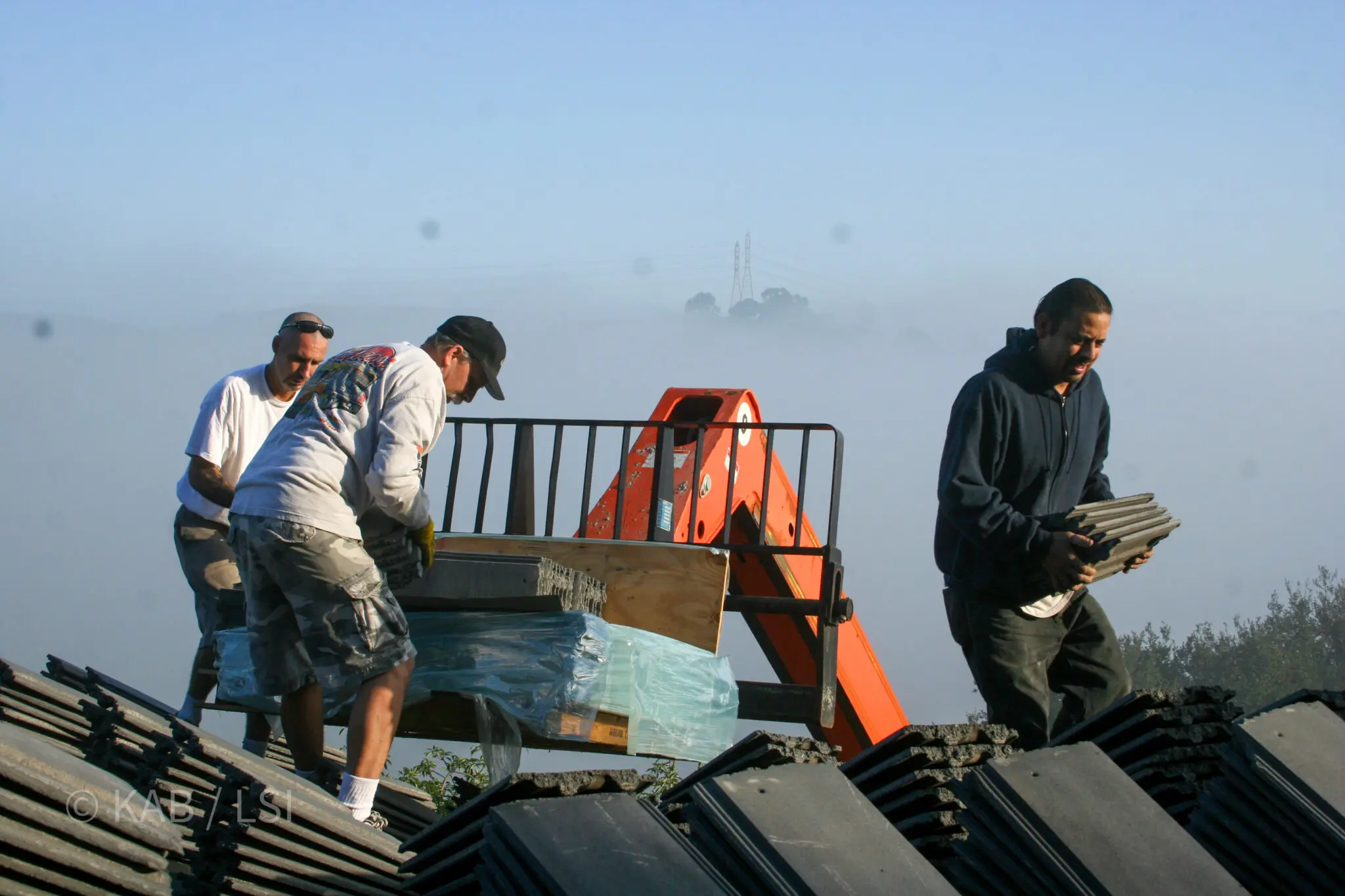 Crew unloading fire-resistant concrete roof tiles in early morning fog on the hills © KAB/LSI