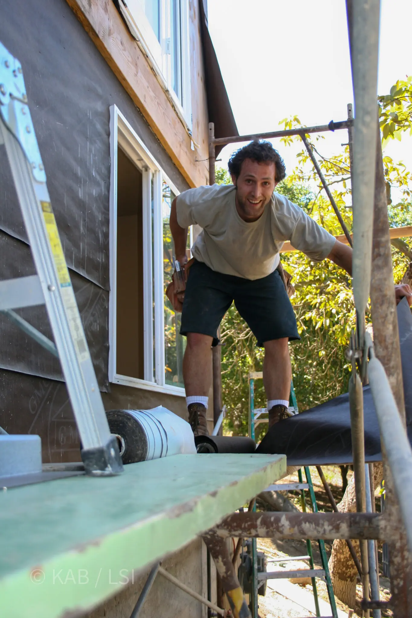 A young pastor on scaffolding at a La Habra Heights hillside home, smiling while learning the stucco trade during a whole-house exterior restoration