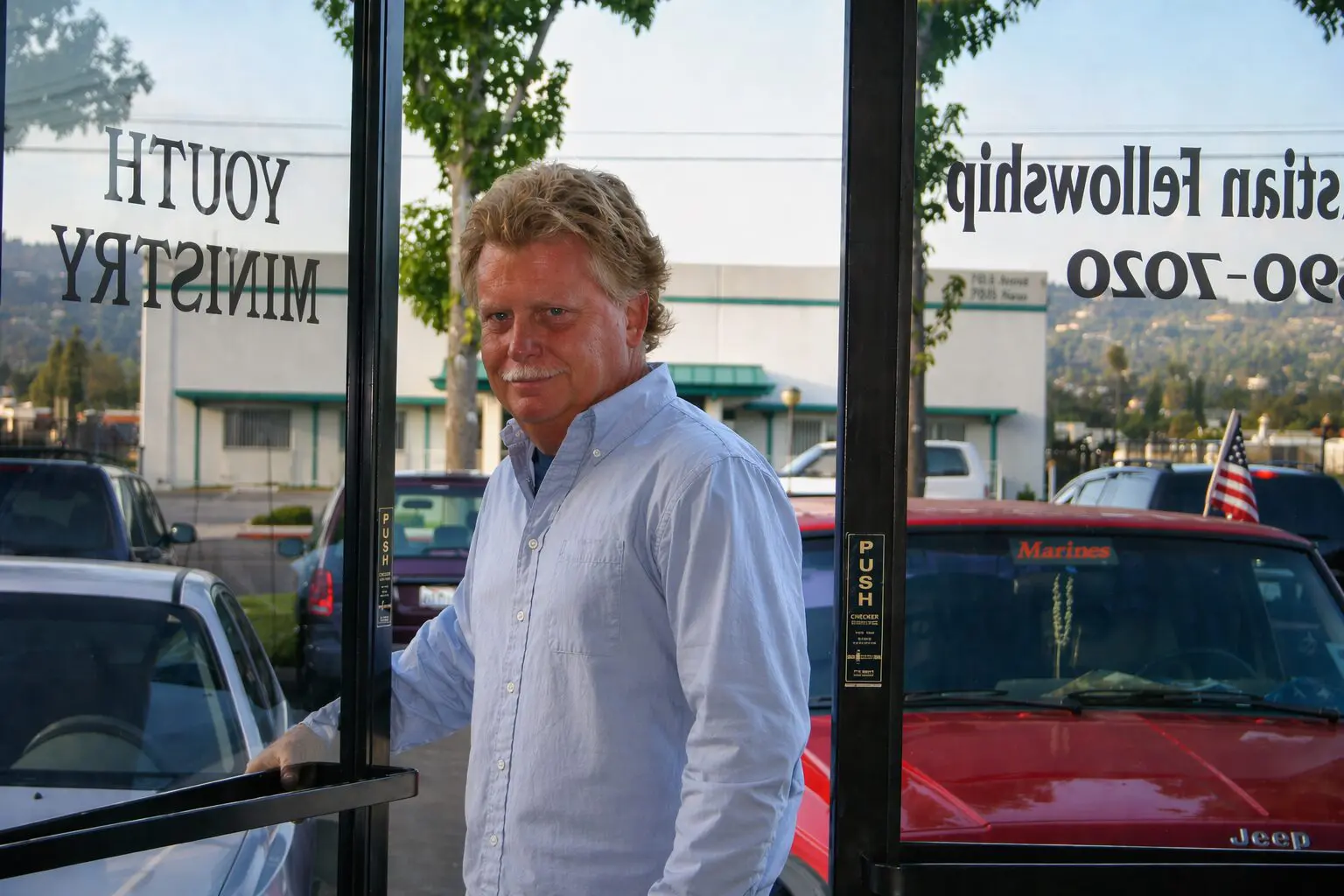 Keith Bennett standing at the glass-door entrance of a Christian Fellowship building, the words YOUTH MINISTRY visible reversed on the glass behind him. Mid-2000s.