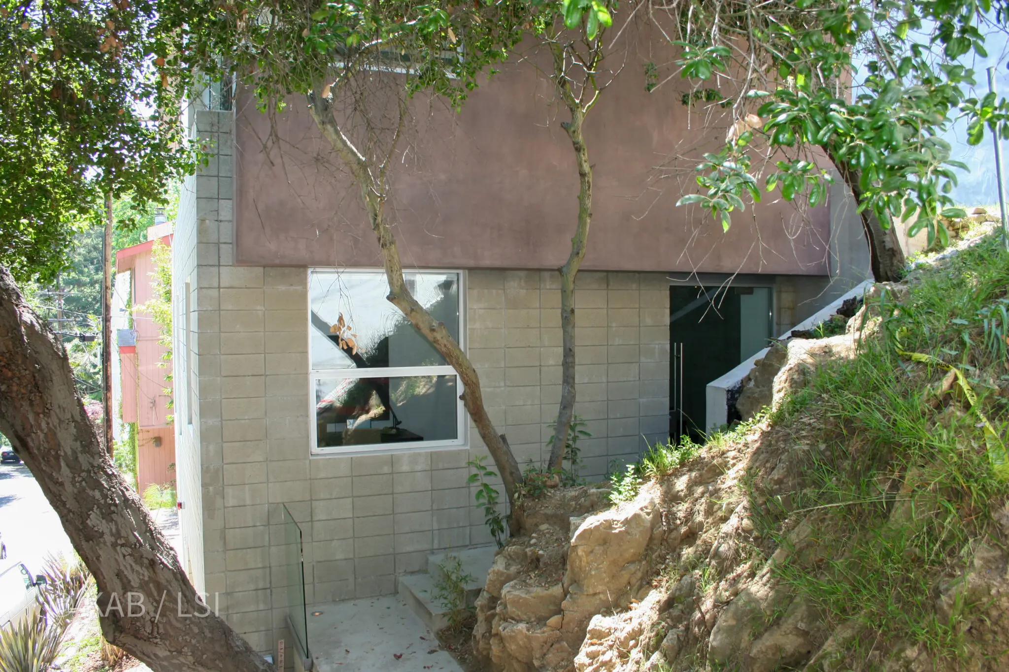 Modern hillside home preserving mature trees and native bedrock beside a neighboring lot cut into granite