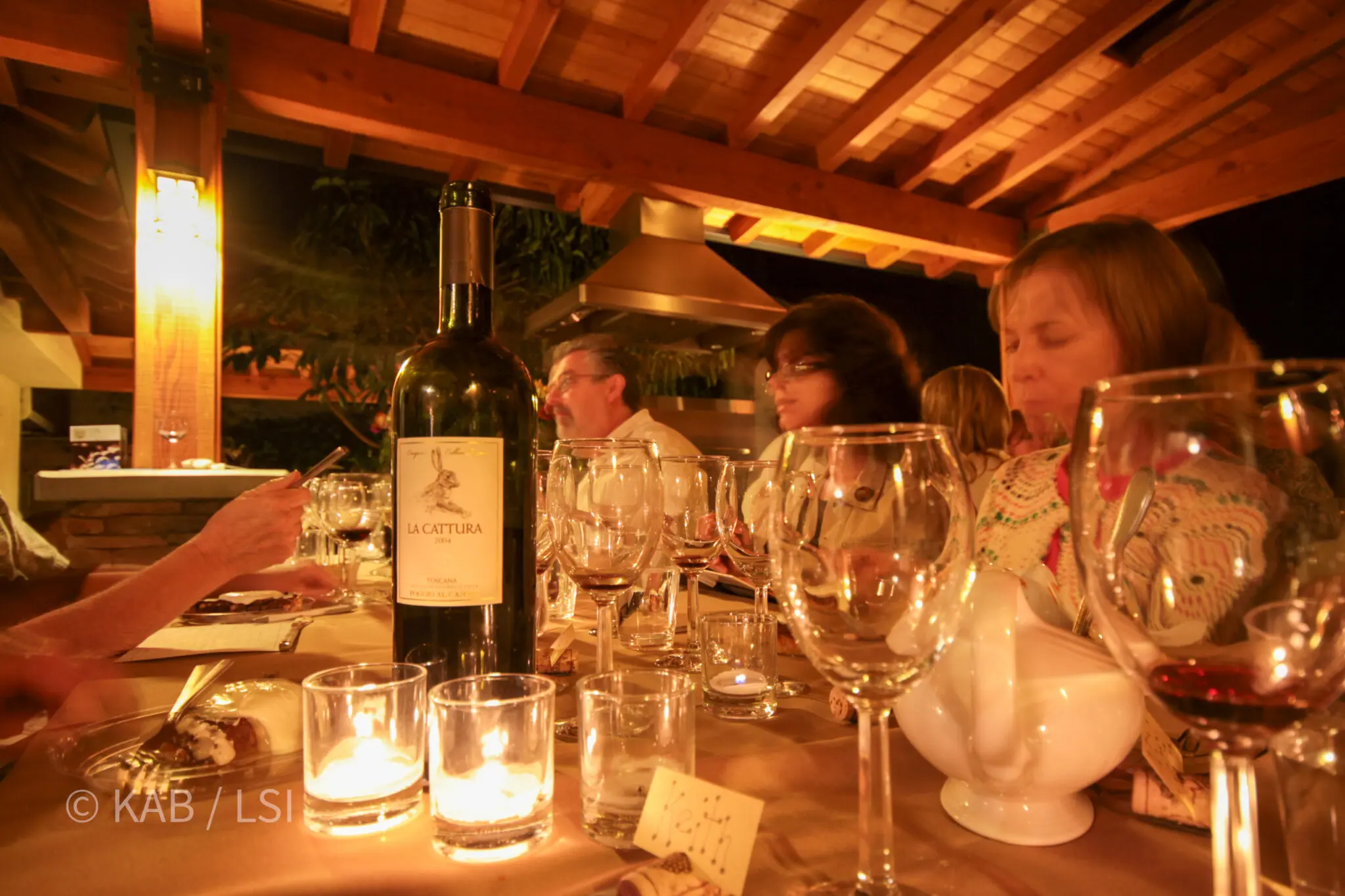 Outdoor dinner party at dusk on a La Habra Heights pergola property — candlelit table set for a wine tasting with neighbors and friends gathered around