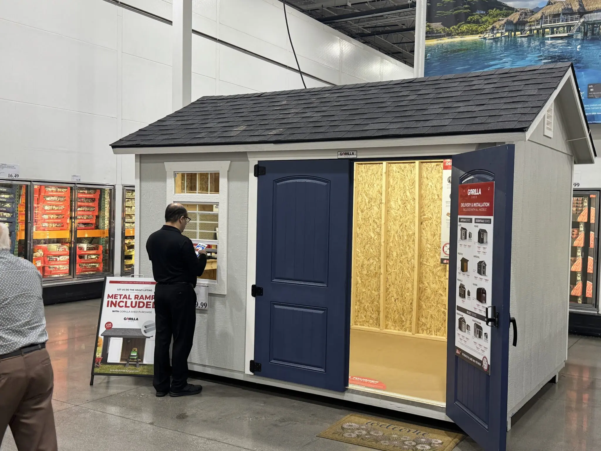Gorilla Premium wood-framed storage shed on Costco display with navy doors, shingled gambrel roof, and Metal Ramp Included sale sign