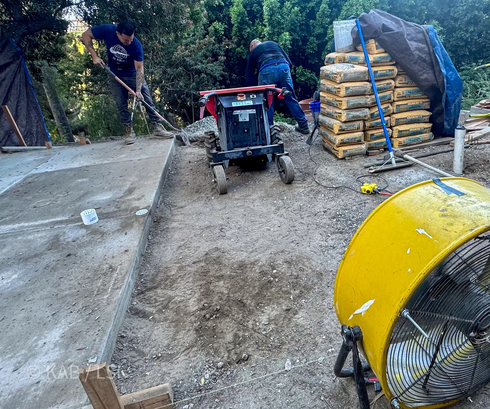 Workers mixing concrete on site with a portable mixer and bagged material for a small hillside pad pour on a hillside property in La Habra Heights