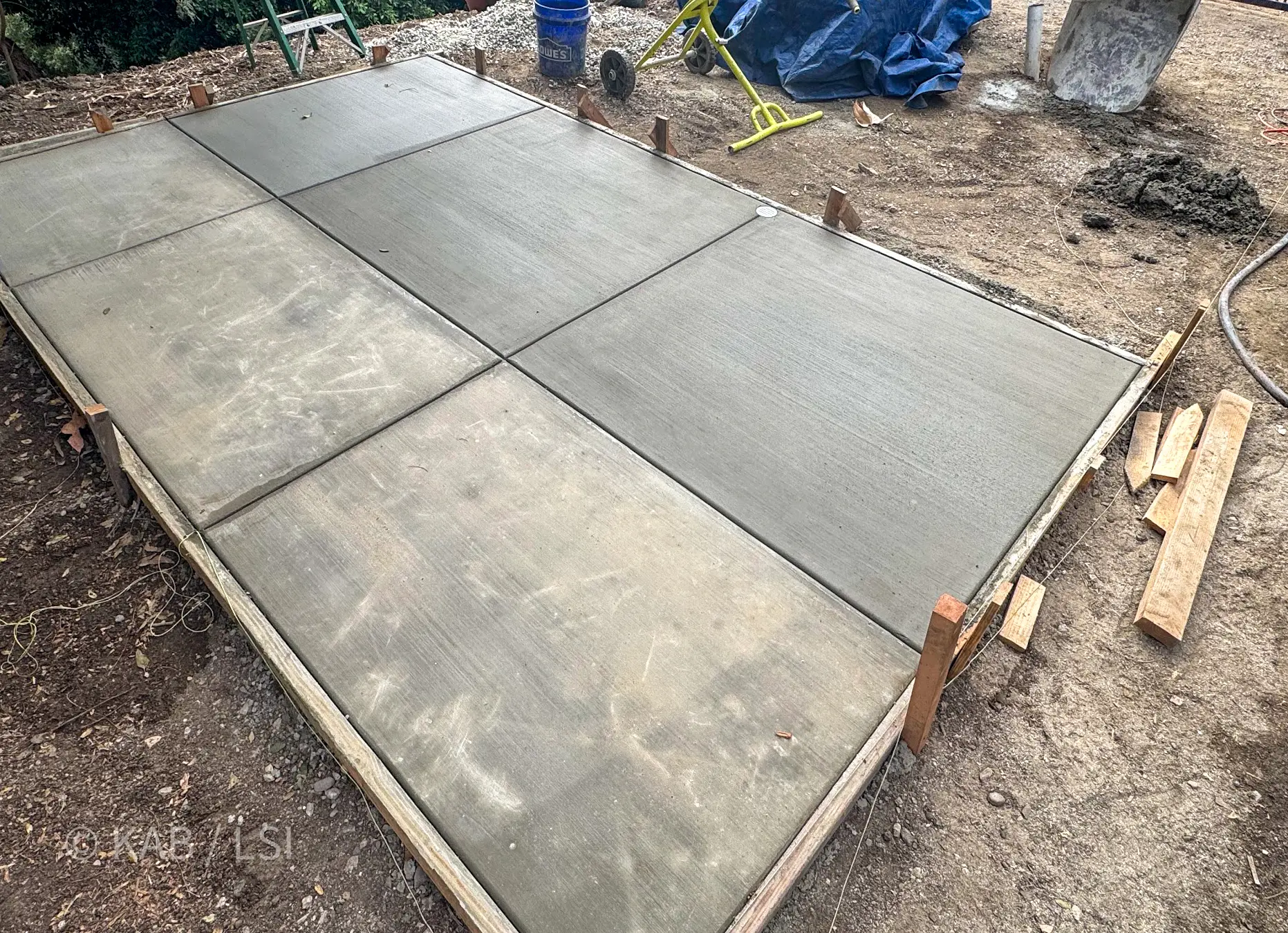 Freshly poured and screeded concrete pad held in timber forms on a sloping hillside lot