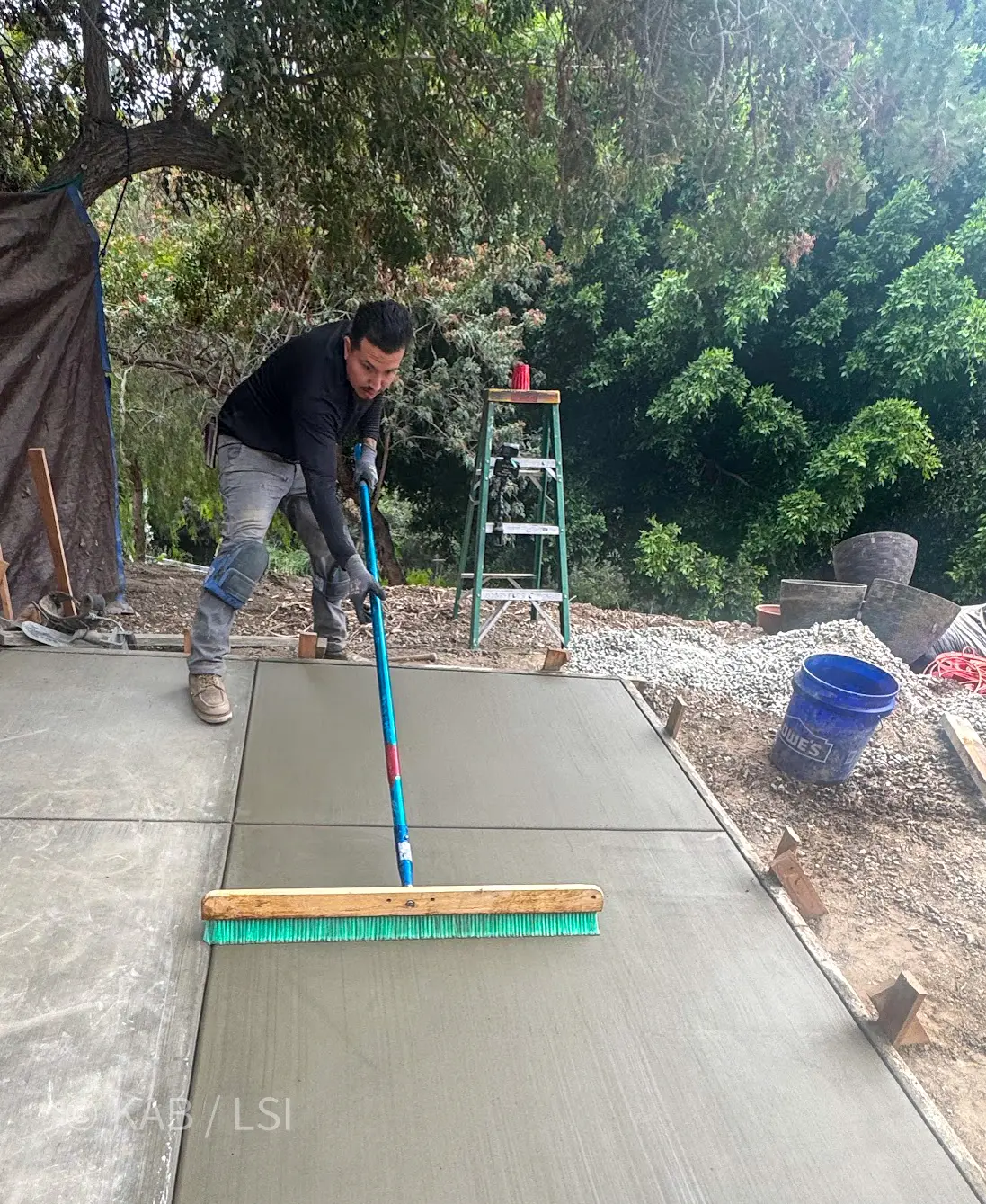 Worker finishing a fresh concrete slab with a long-handled bull float on a hillside property in La Habra Heights