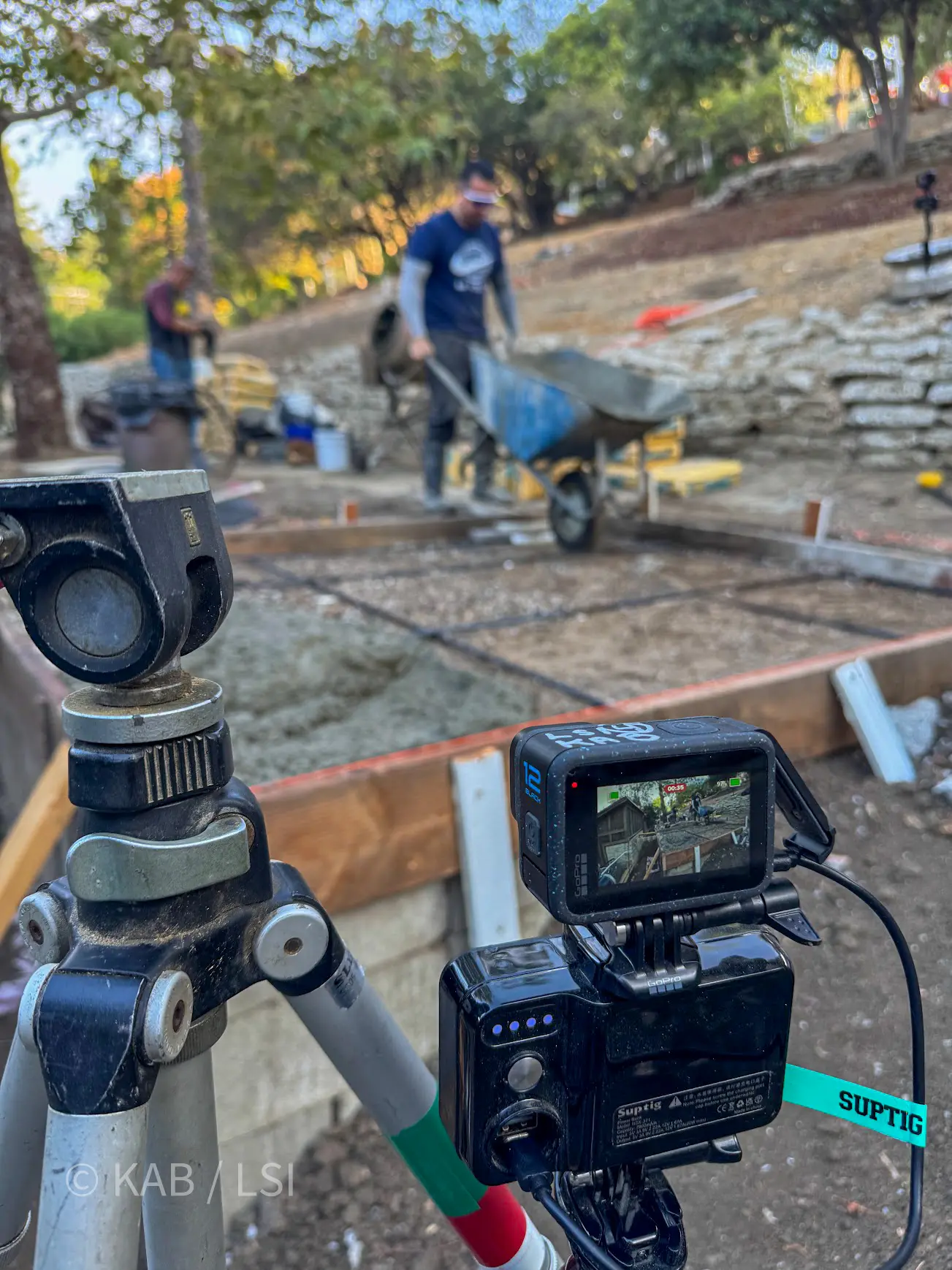 GoPro on tripod with battery pack watching a concrete pour, live feed visible on the camera screen