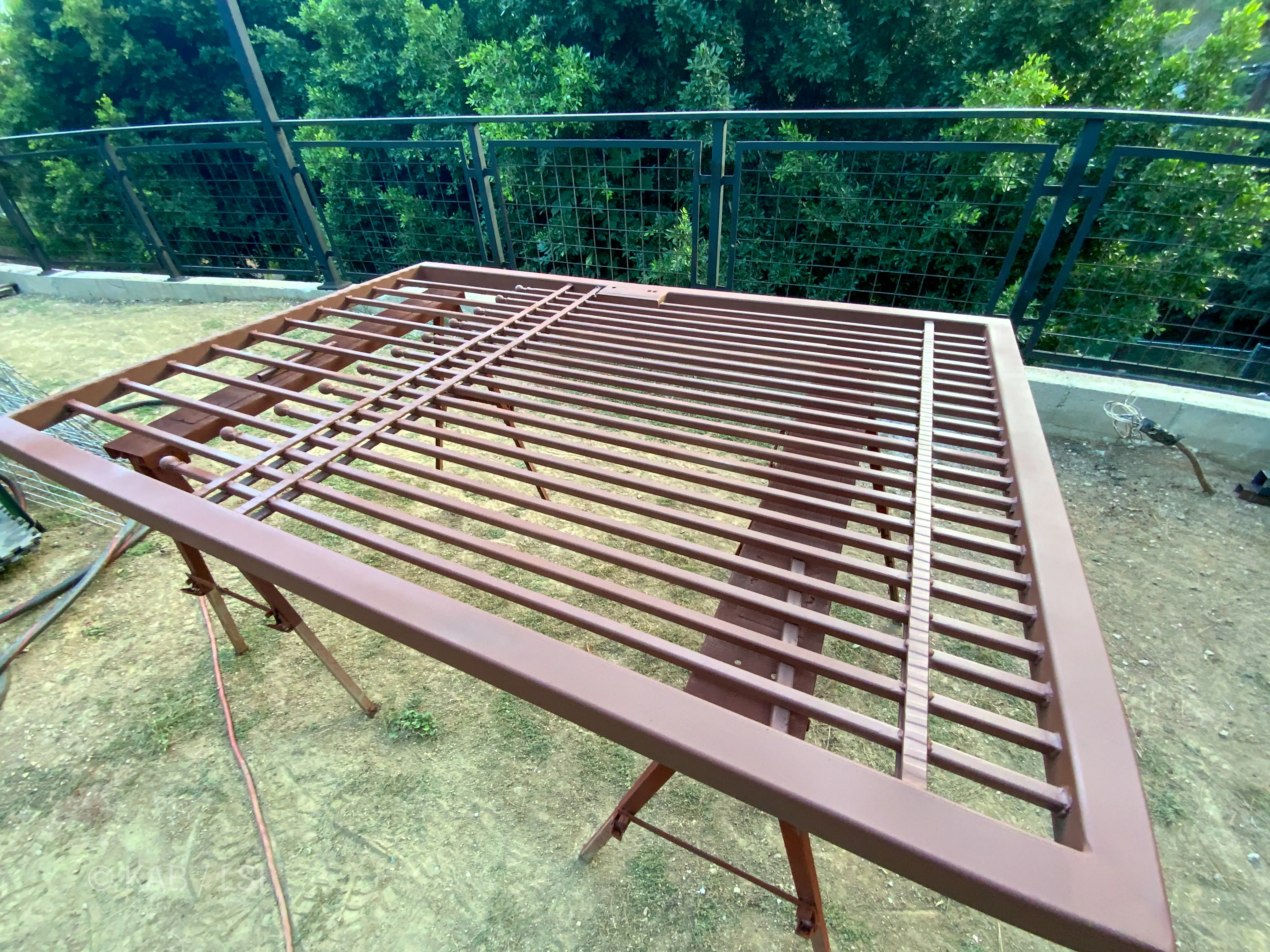 An on-site wrought-iron gate primed in red-oxide metal primer on a La Habra Heights hillside, ready for its finish coat.