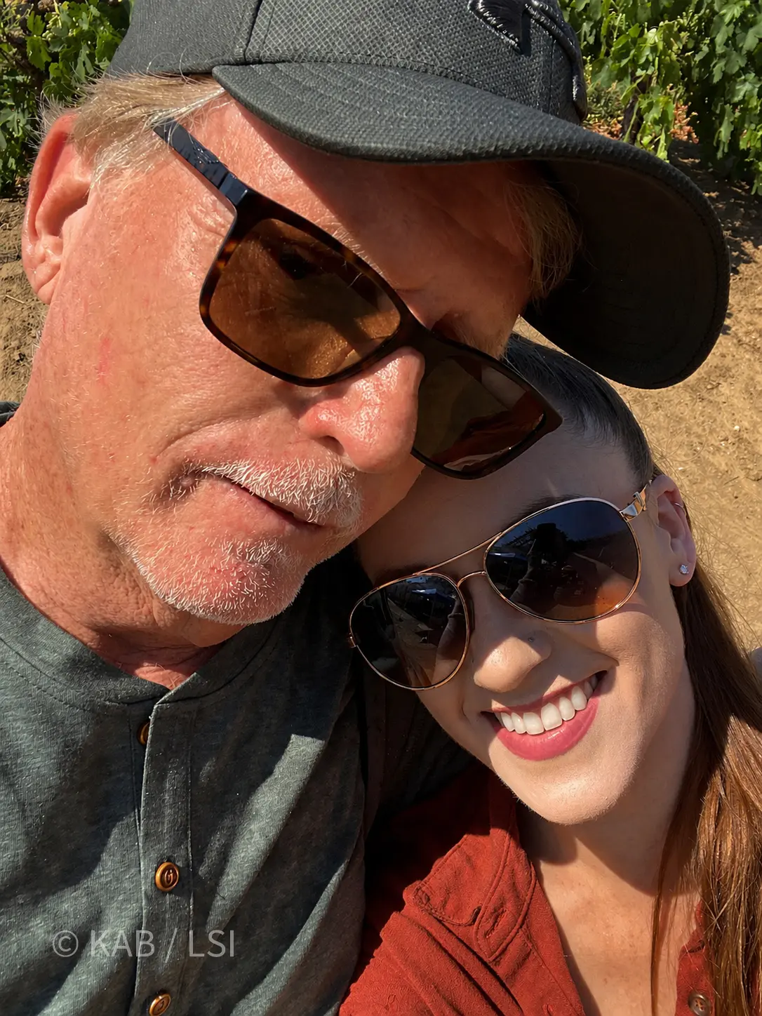Keith Bennett and his daughter Megan Bennett in a close father-daughter selfie in a Temecula vineyard, both in sunglasses, vines visible behind them.