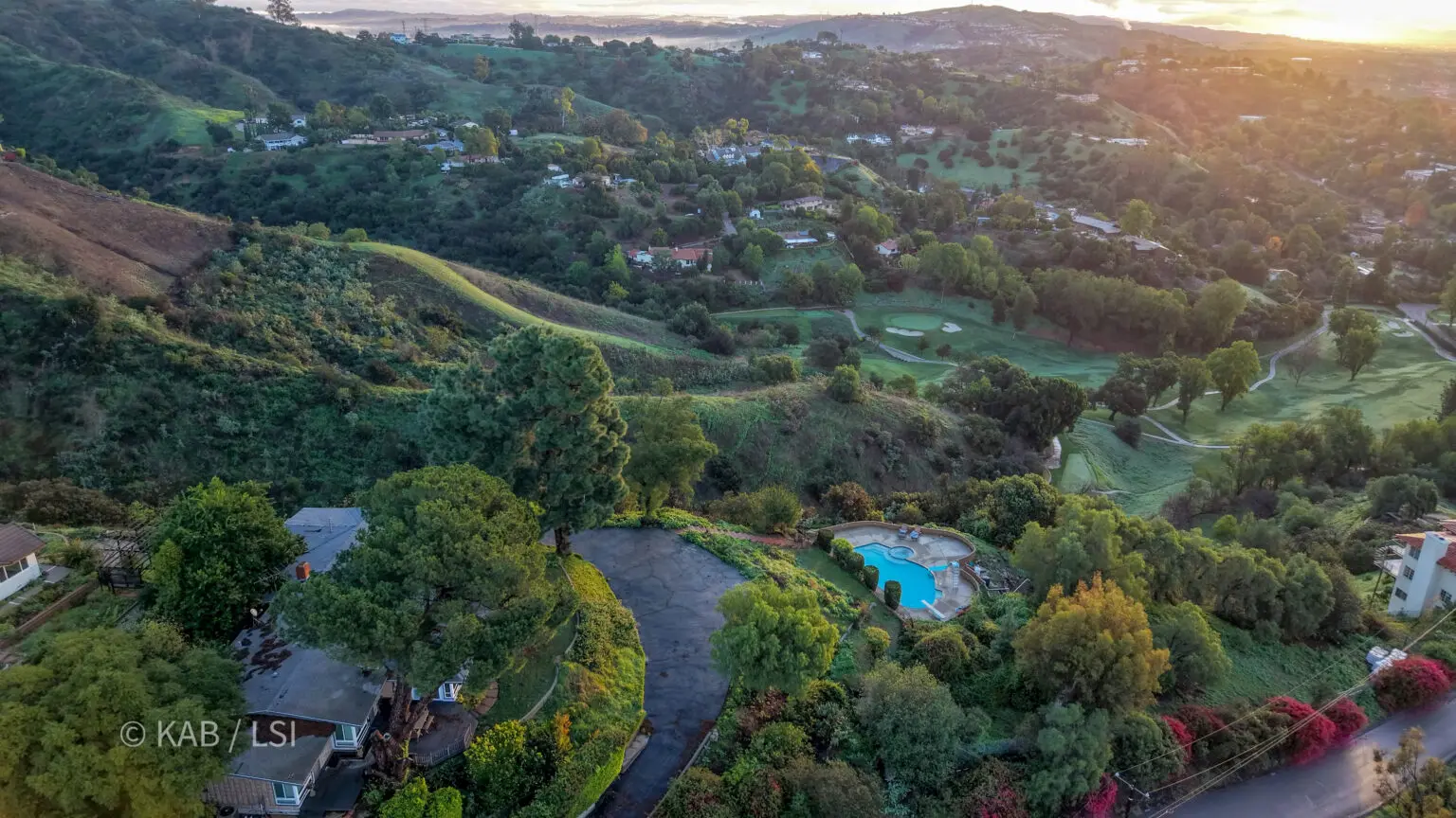The edge of a La Habra Heights canyon at sunrise, hillside homes among trees with the valley opening below.