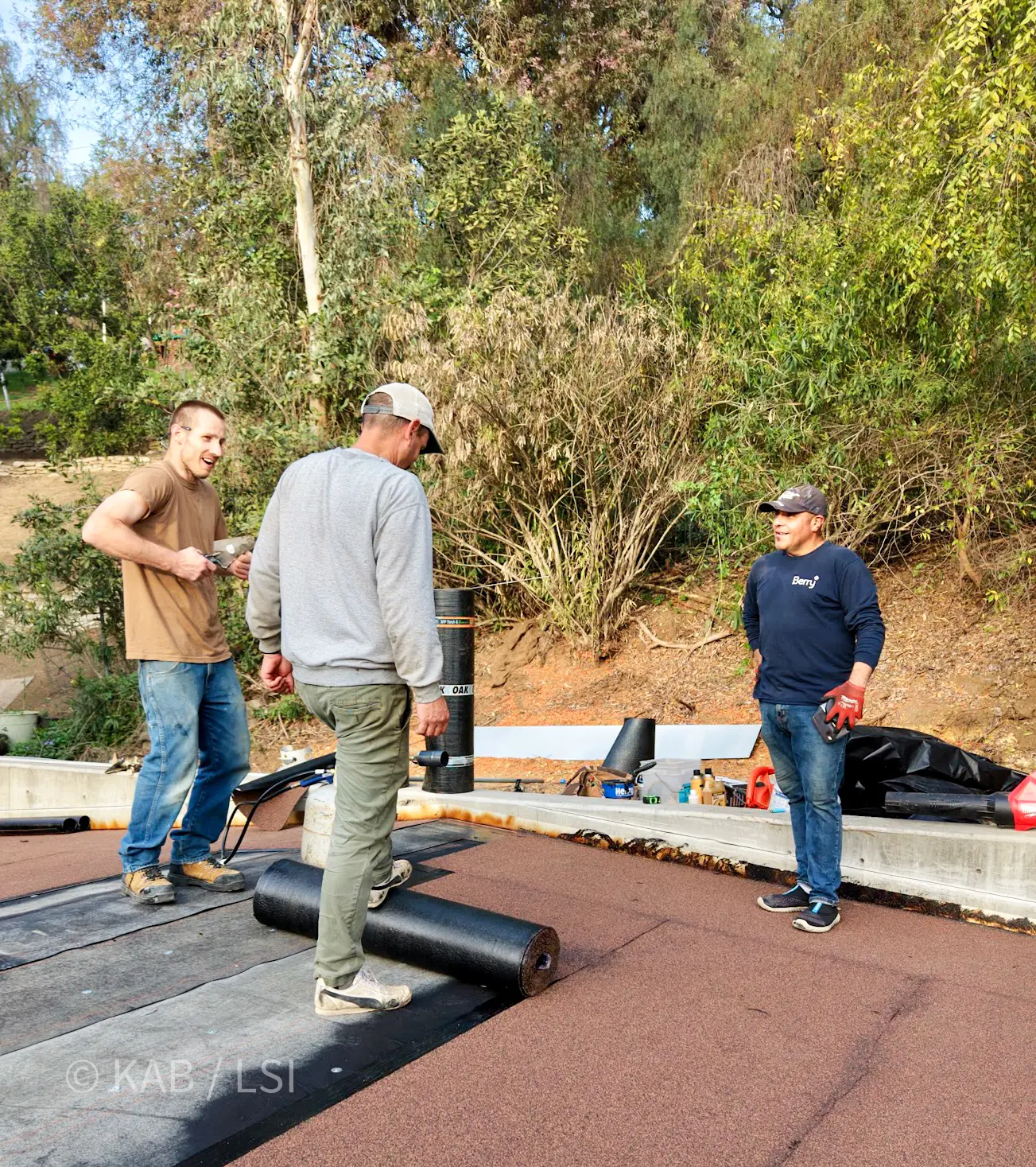 A La Habra Heights homeowner-led crew completing a torch-down roof on a hillside outbuilding before the storm arrives, viewed from above by drone