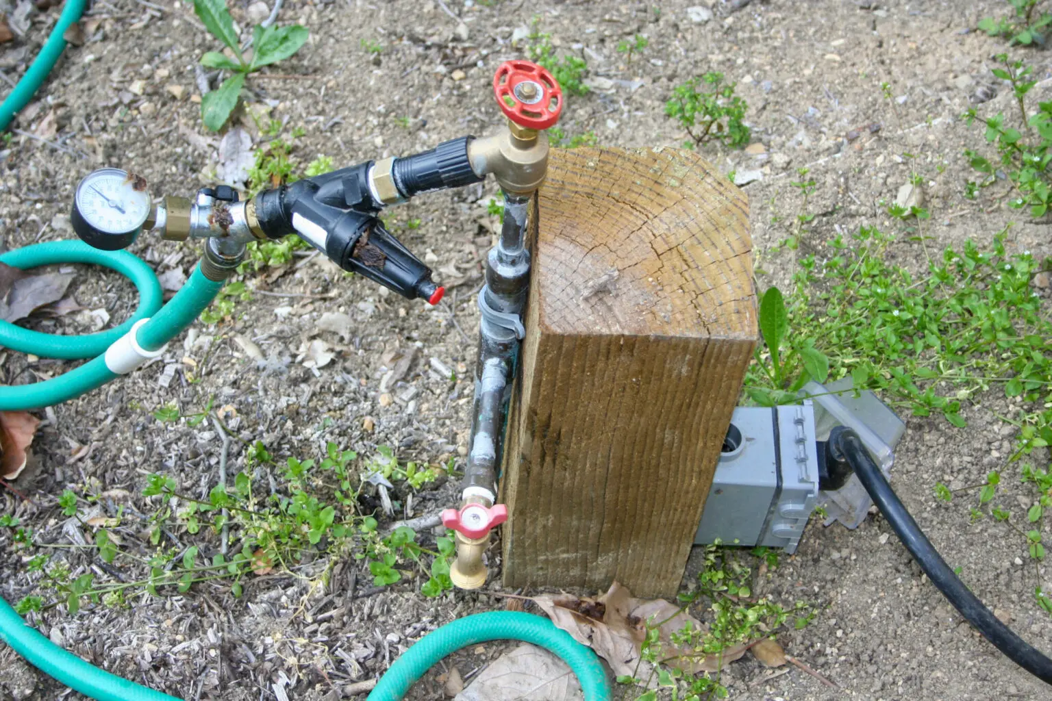 Outdoor water station on a pressure-treated post with a pressure gauge and shutoff valve running at full city pressure, with an electrical box alongside