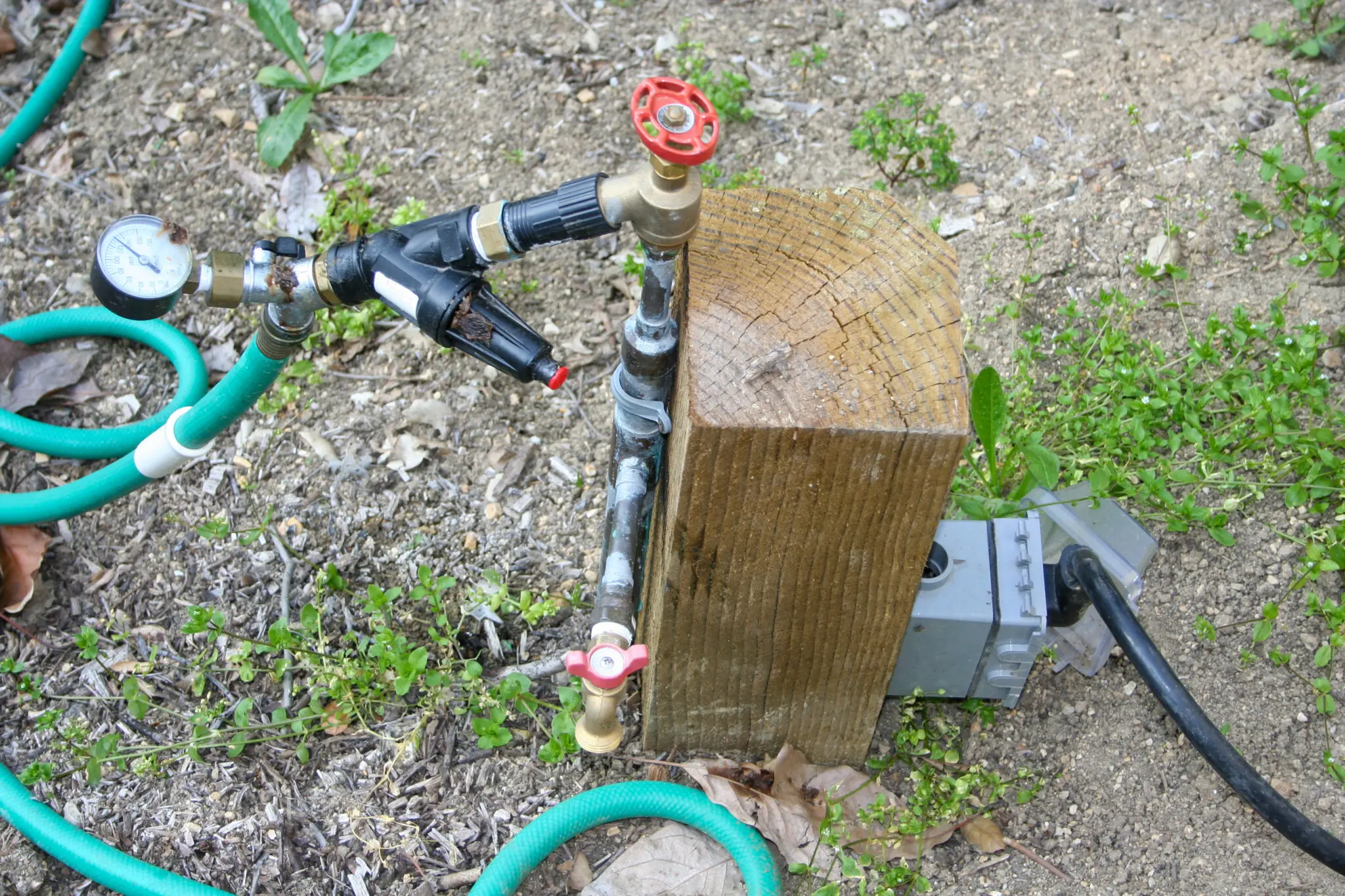 Low-profile Water and Power Station on a La Habra Heights hillside property: pressure-treated post with Type L copper riser, brass inlet valve, pressure gauge, pressure regulator, secondary brass outlet valve, and a weatherproof electrical outlet integrated on the same fixture