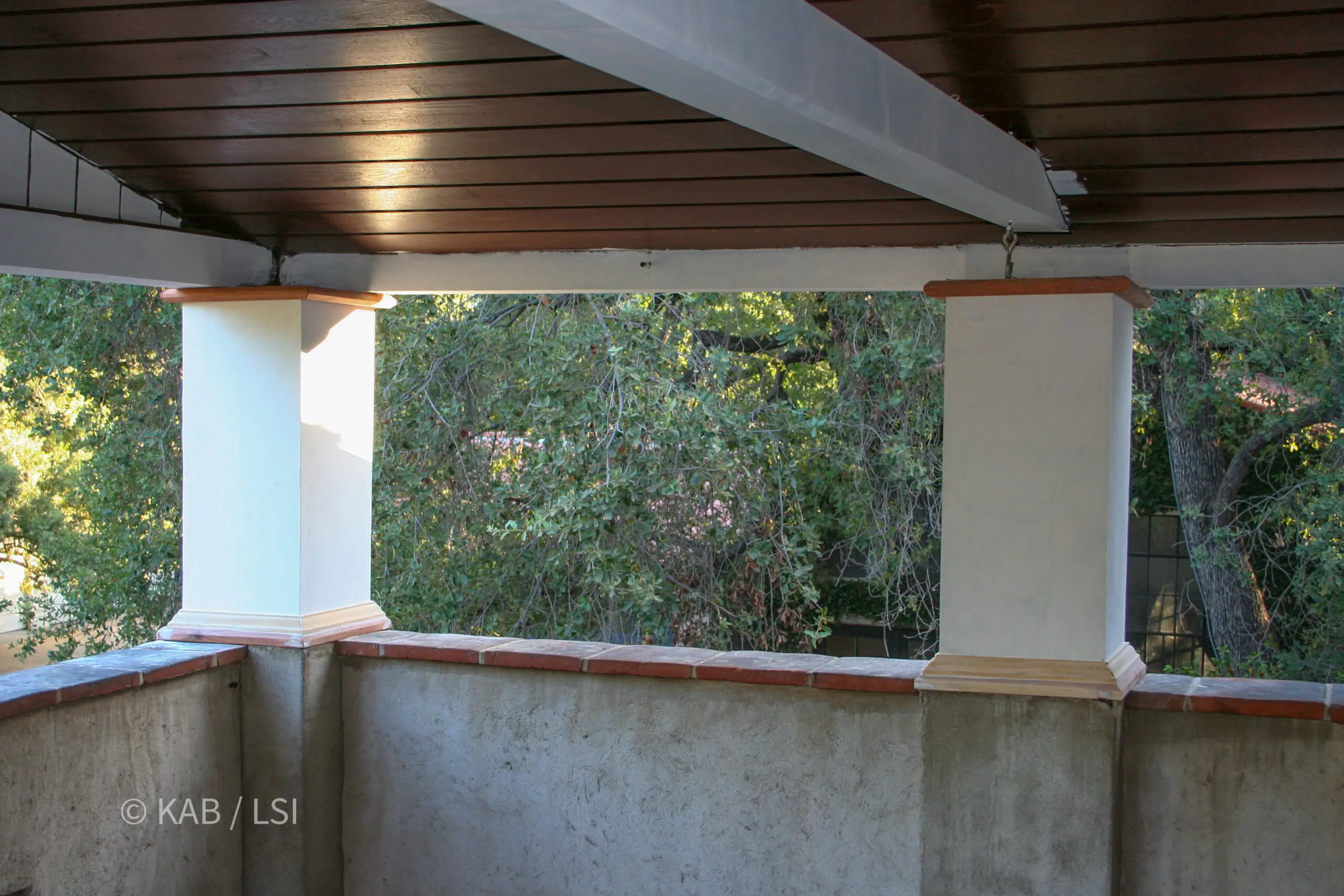 Covered porch with painted columns and a tiled rail looking out into mature oaks on a hillside property