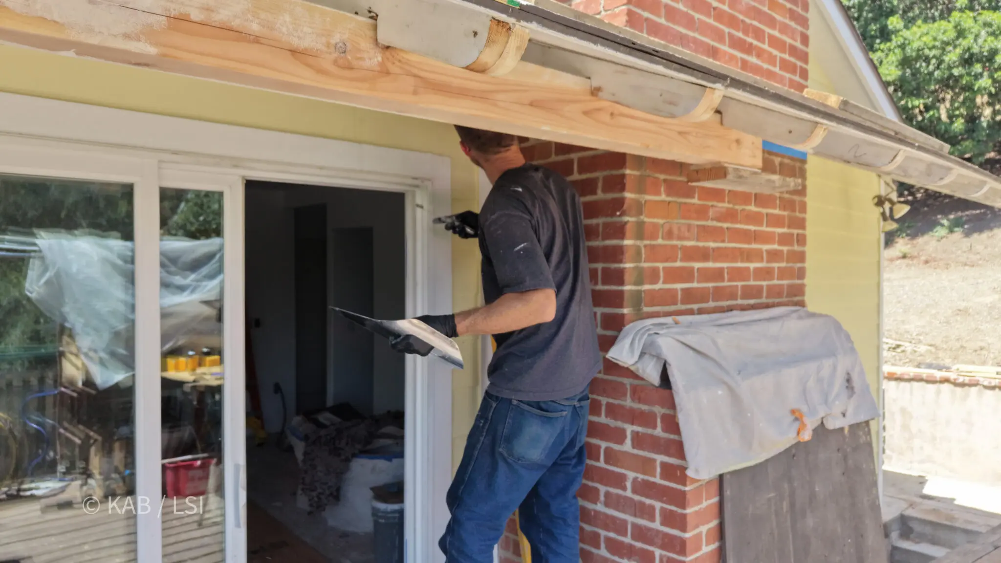 Plasterer troweling a stucco patch beneath newly rebuilt rafter tails and fascia on a hillside home