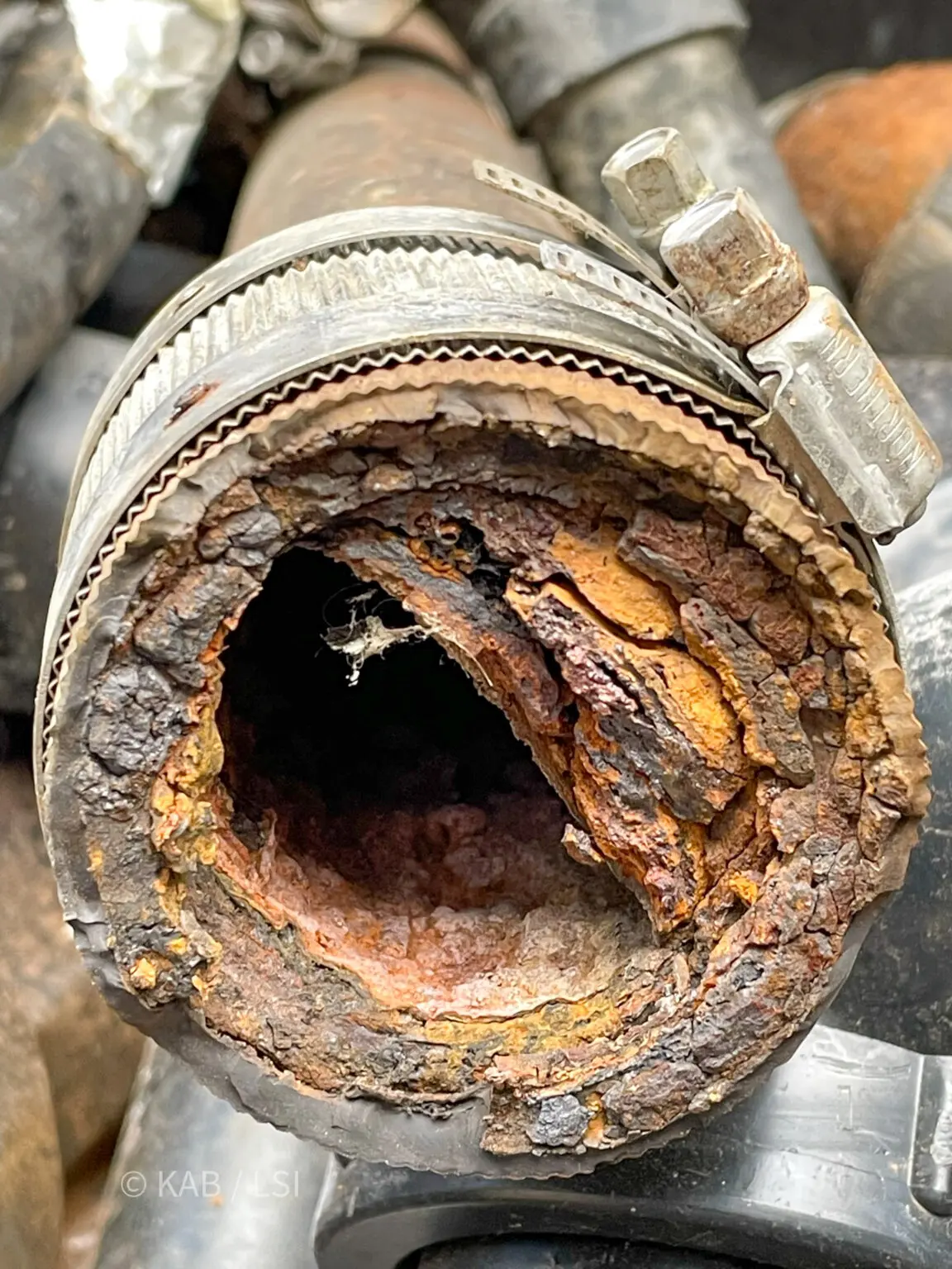 Cross-section of a removed two-inch cast iron drain pipe showing severe internal corrosion that has reduced the opening to under one inch