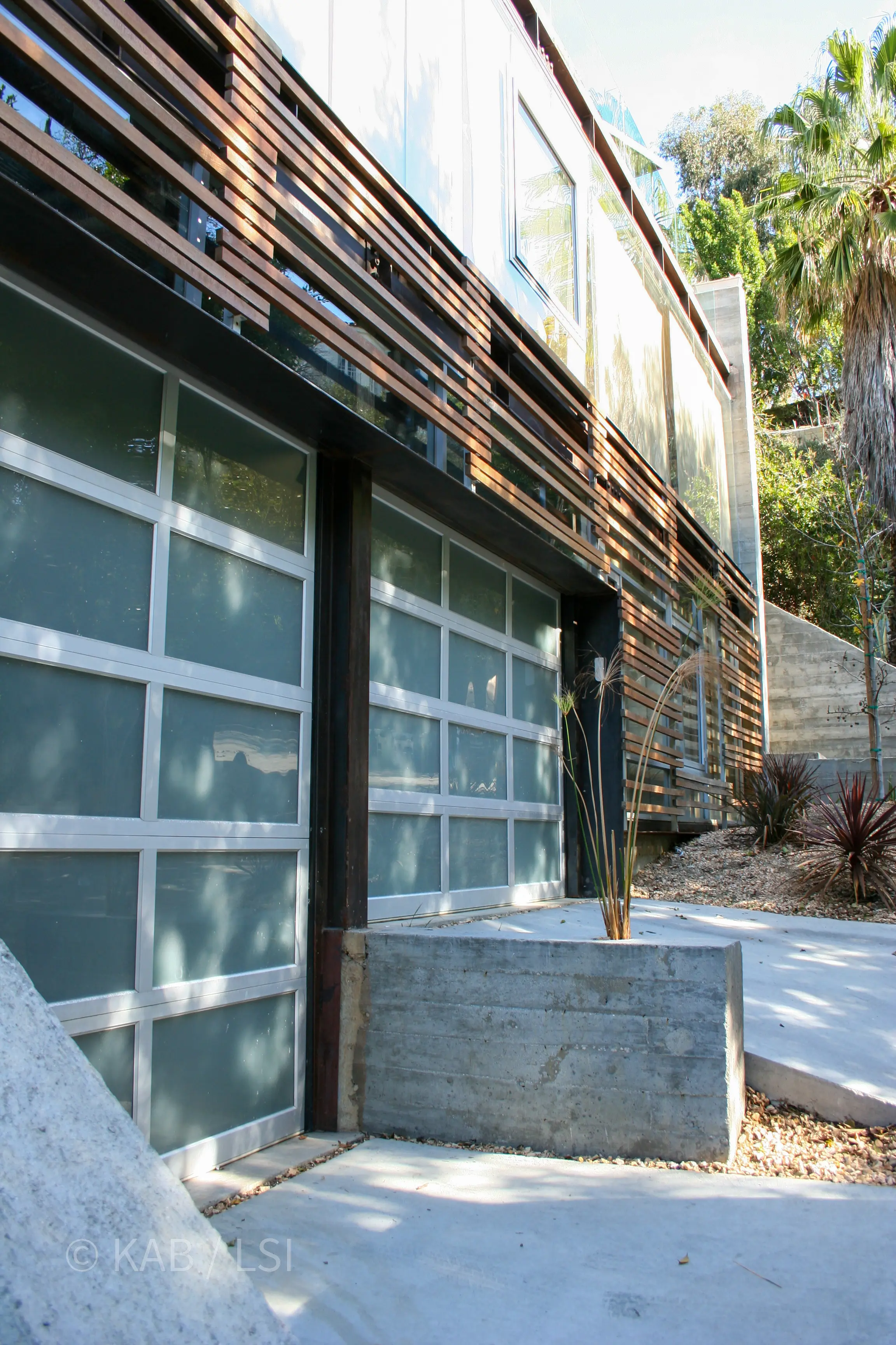 Front elevation of a finished concrete, steel and glass hillside home with warm timber cladding on a narrow canyon street