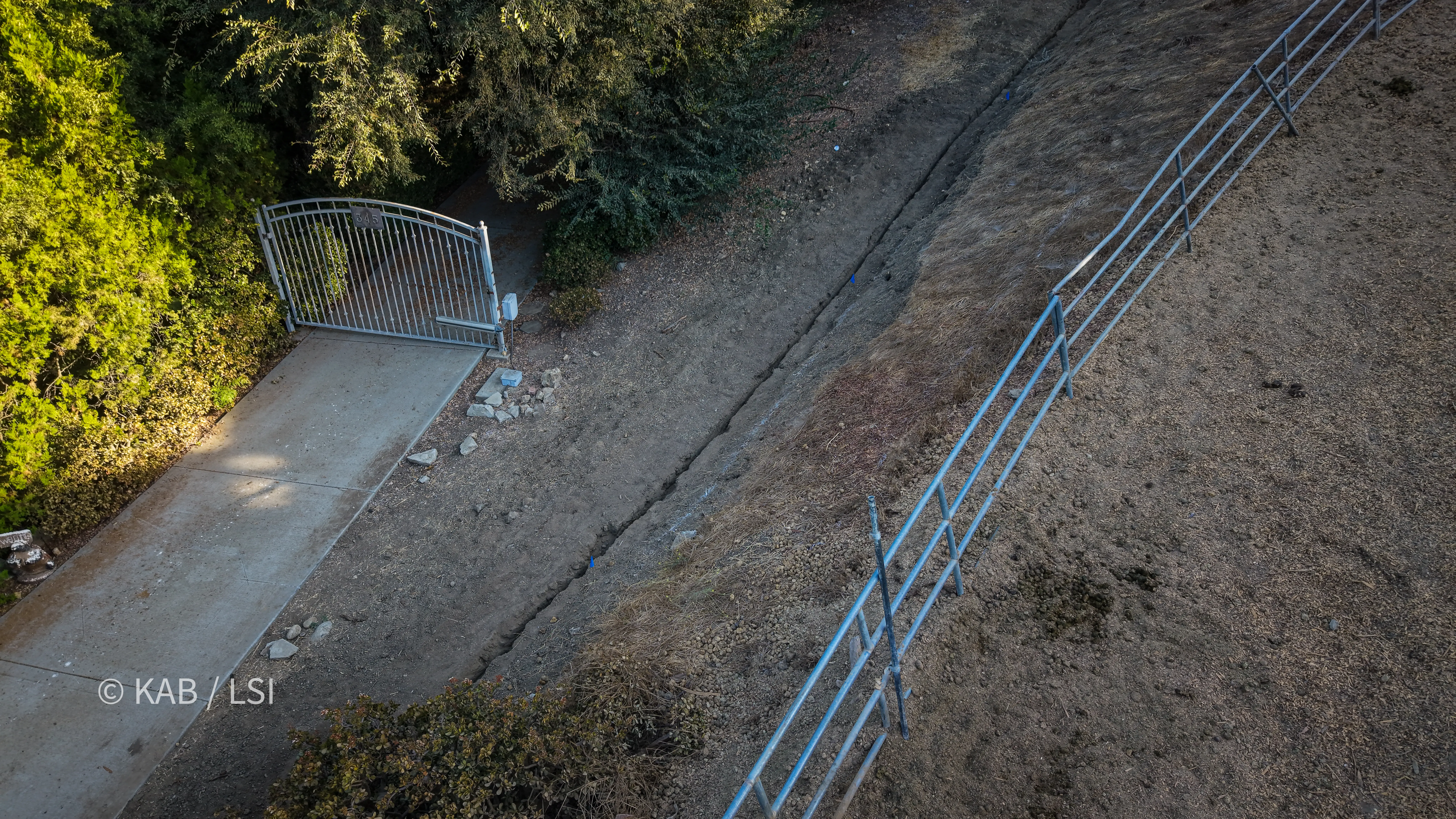 Aerial view of a water service trench running alongside a driveway gate and fence line at the bottom of a hillside property