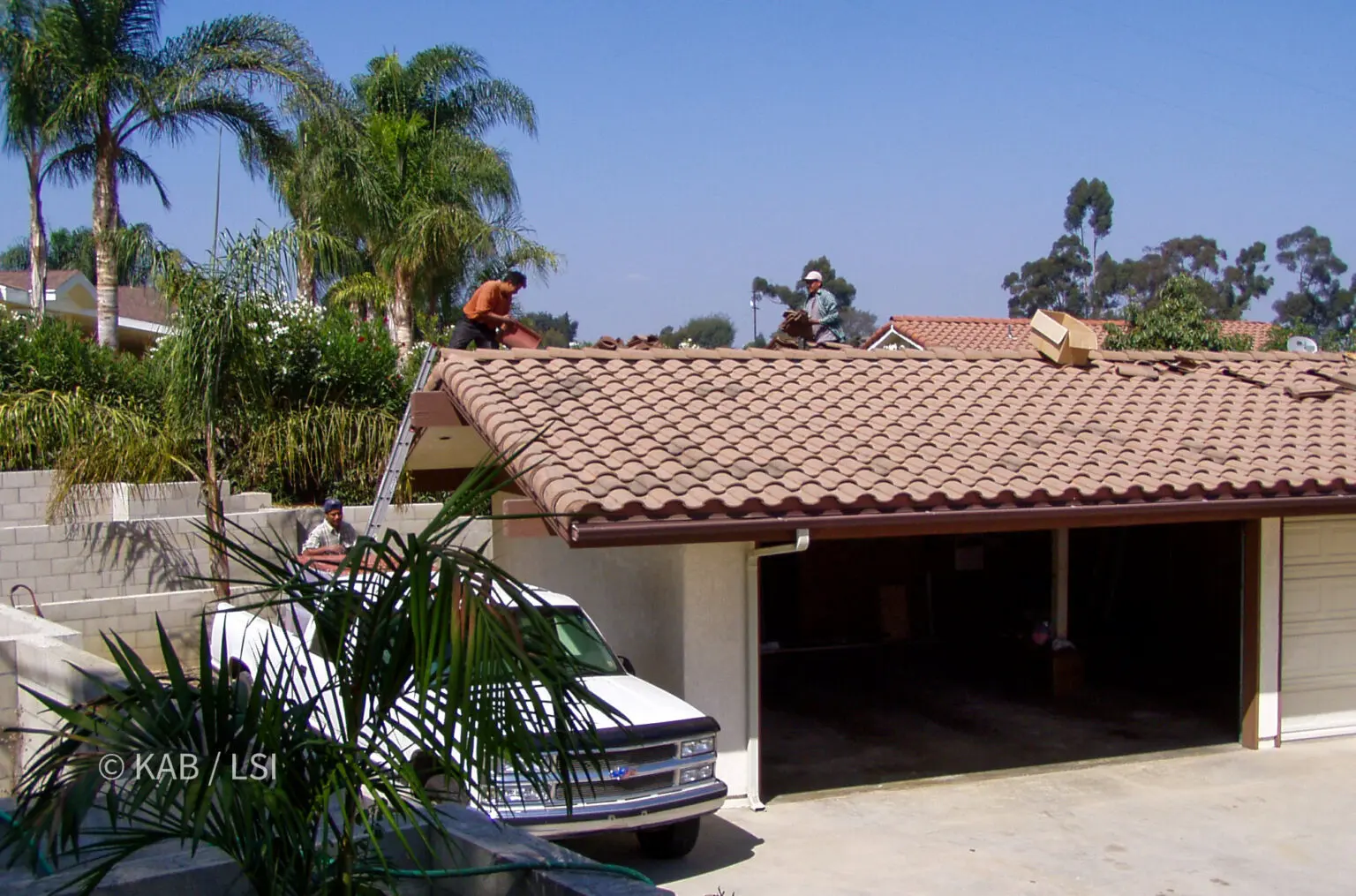 Roofers reinstalling concrete tile on the garage roof of a hillside home in La Habra Heights