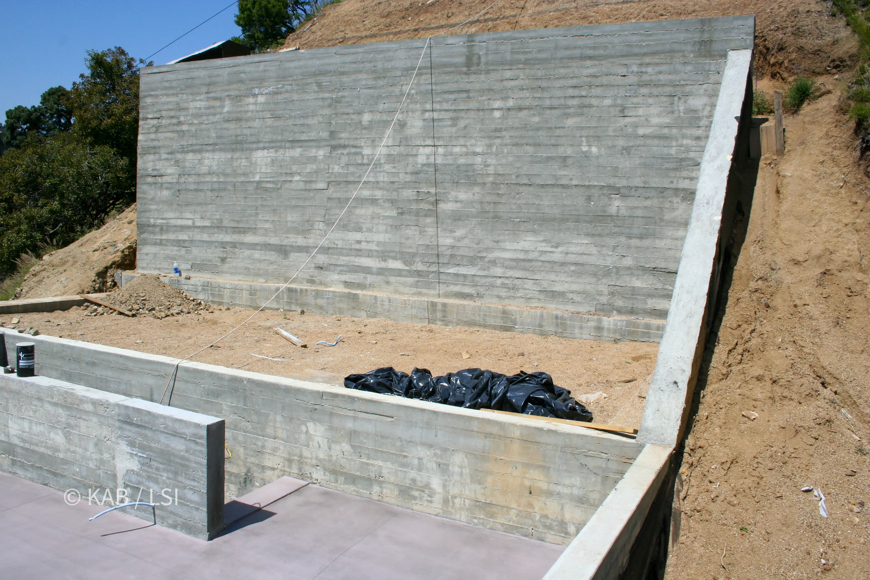 Twelve-inch board-formed concrete wall forming the third story and rock-fall protection of a hillside home above a canyon