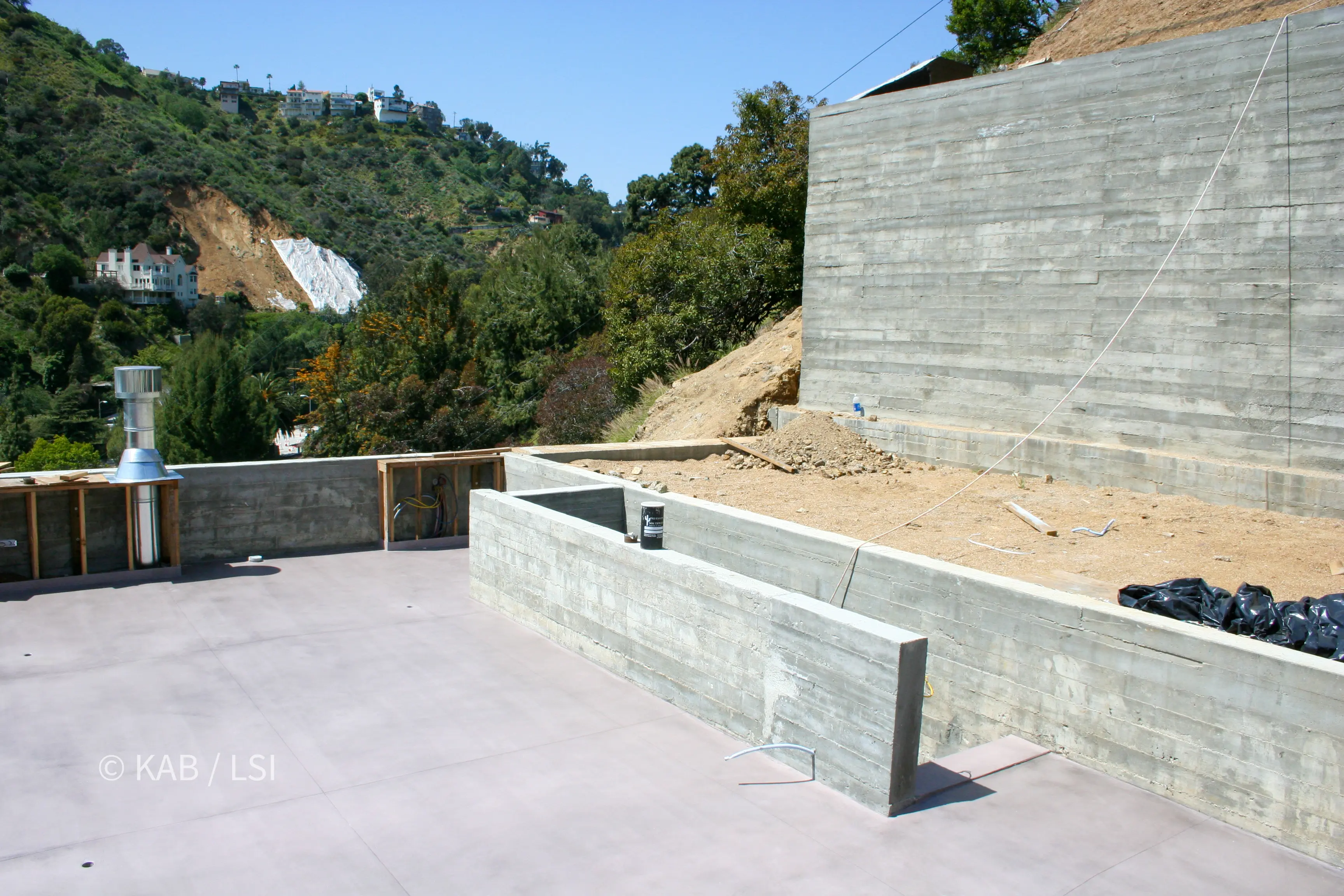 Rooftop deck enclosed by a board-formed concrete rock-fall protection wall overlooking a green canyon