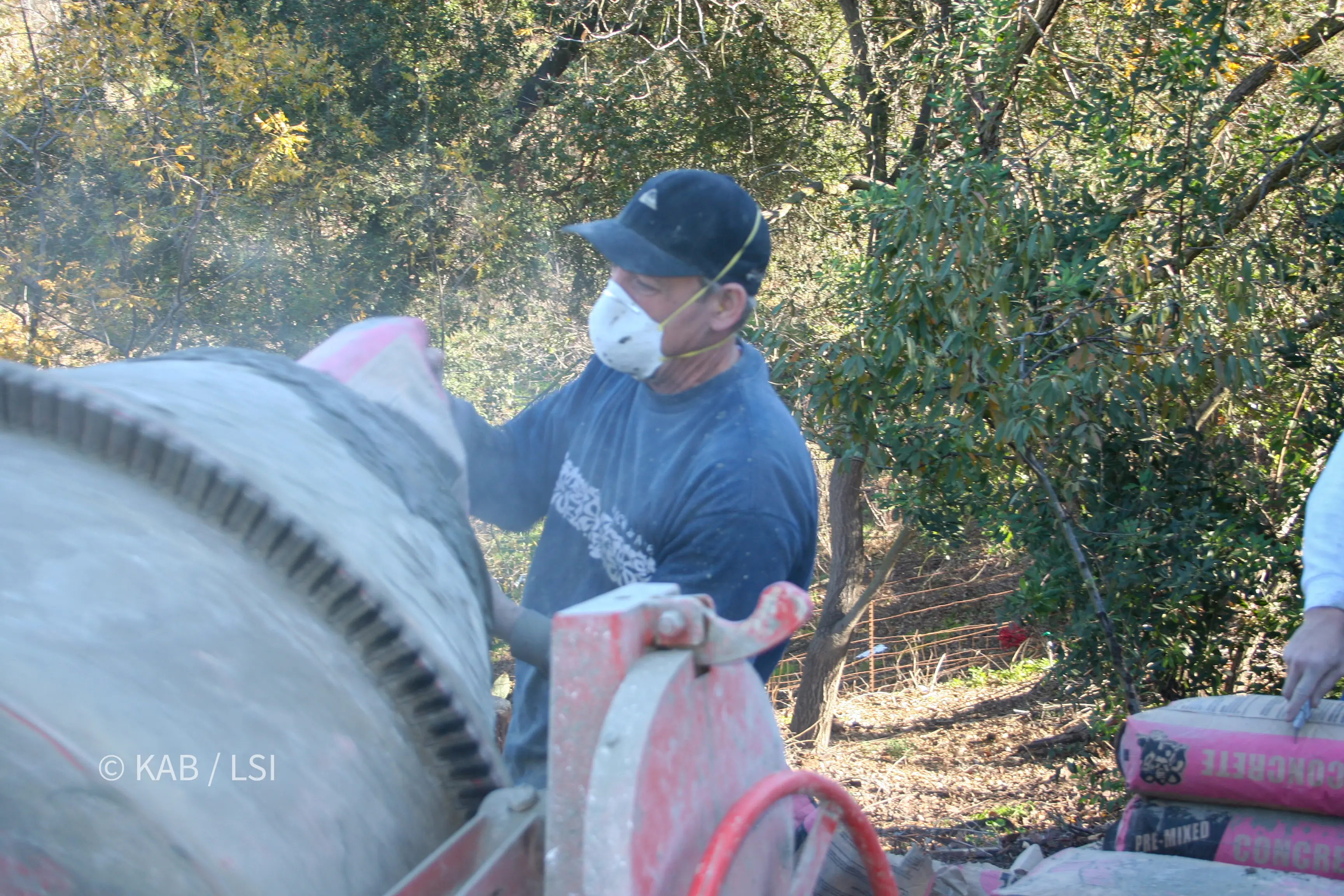 Contractor charging a towable concrete mixer with bagged pre-mixed concrete on a hillside property in La Habra Heights