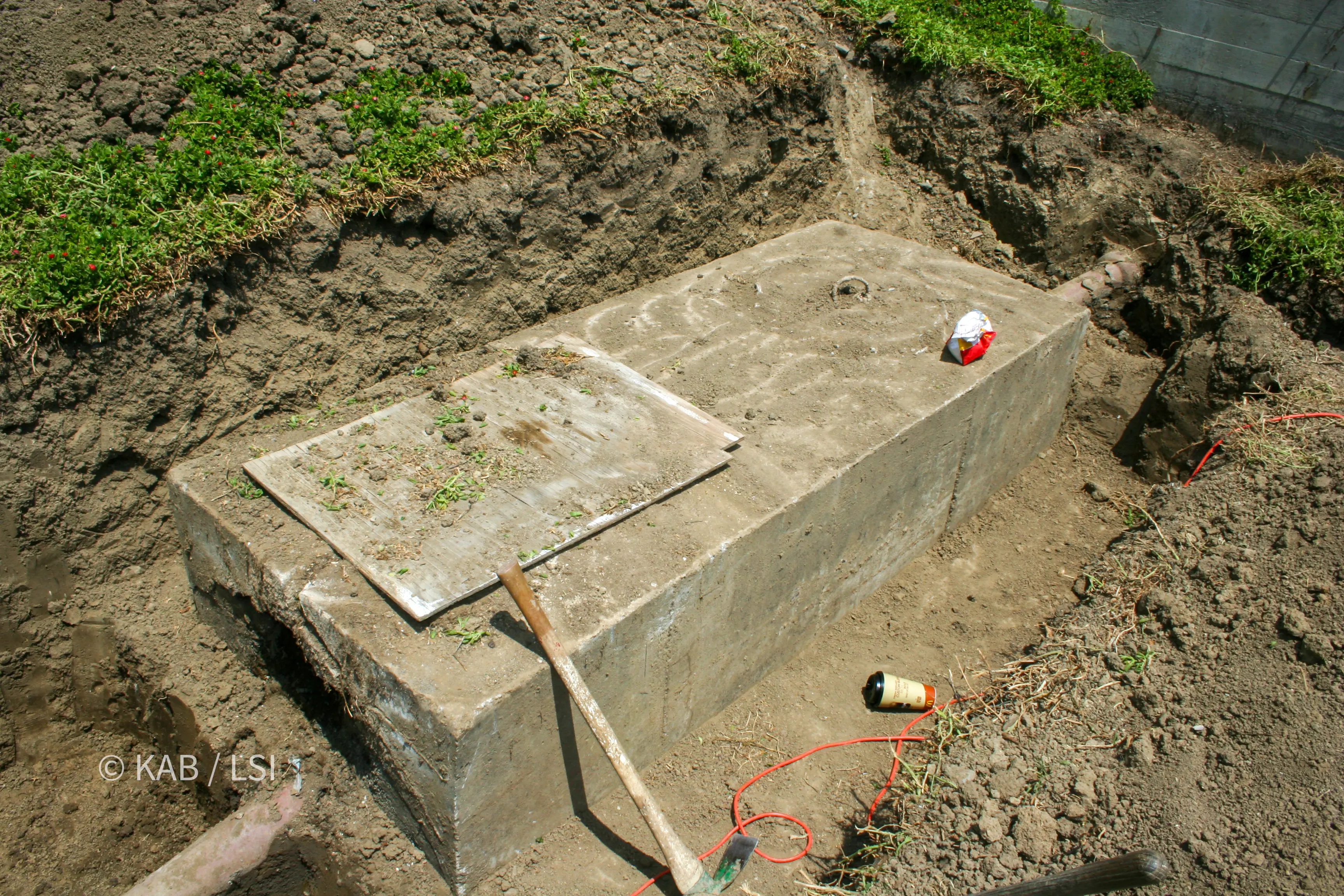 Exposed concrete septic tank lid with the original open-jointed clay pipe running to it