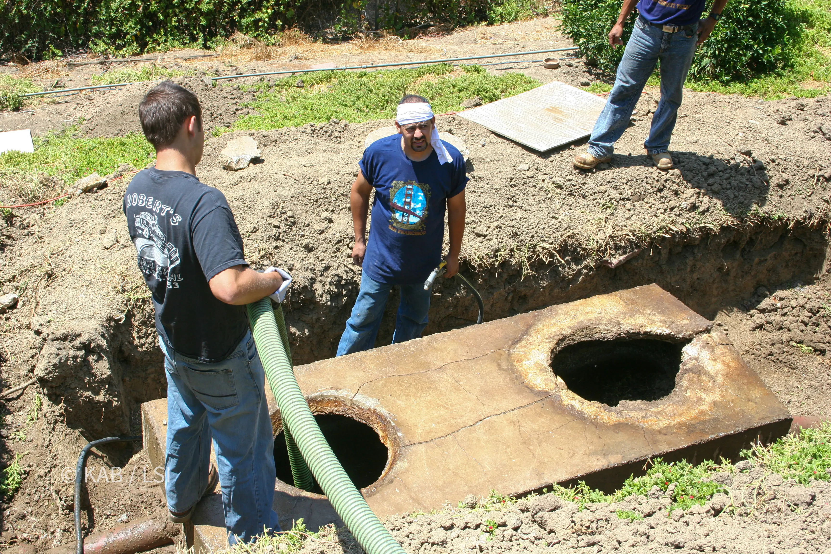 Close view of a 1950s concrete septic tank lid with two open access holes, corroded rings and a crack running between them