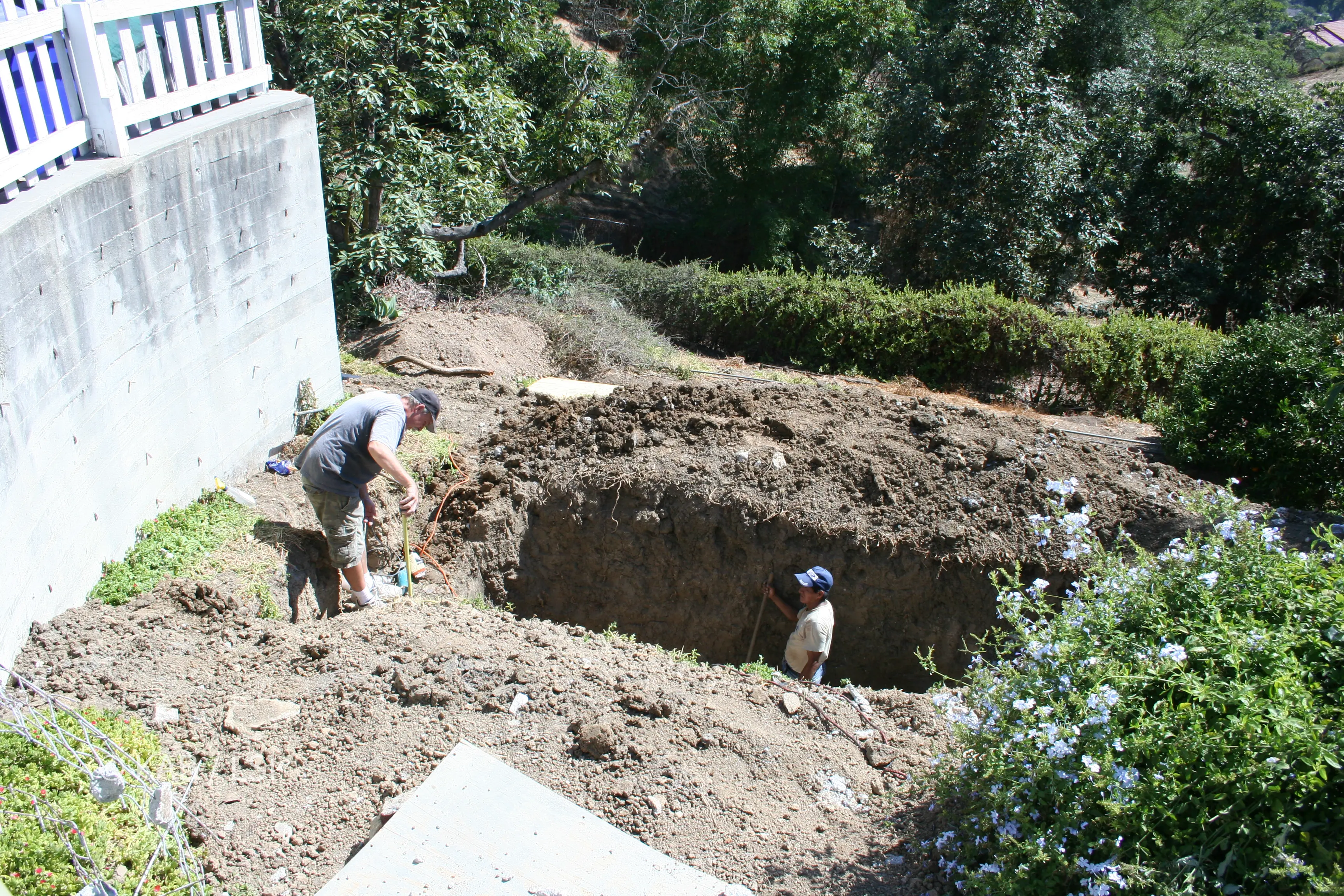 Rectangular excavation dug for a replacement septic tank beside a hillside home