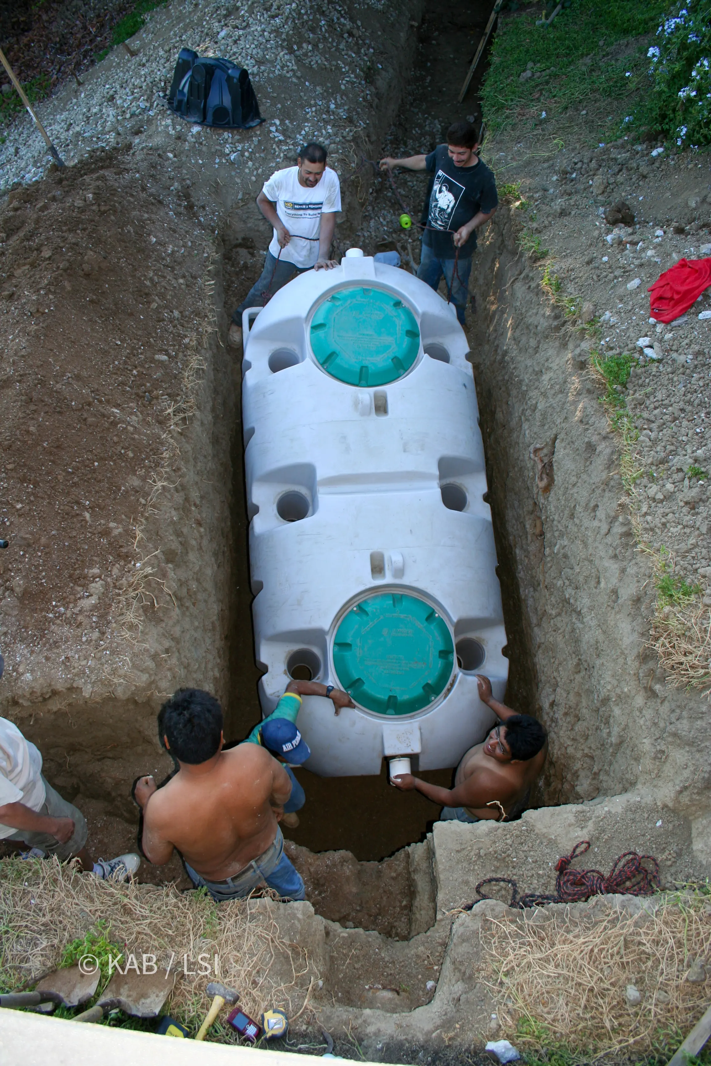 Overhead view of a two-chamber polyethylene septic tank positioned in an excavation with green riser lids