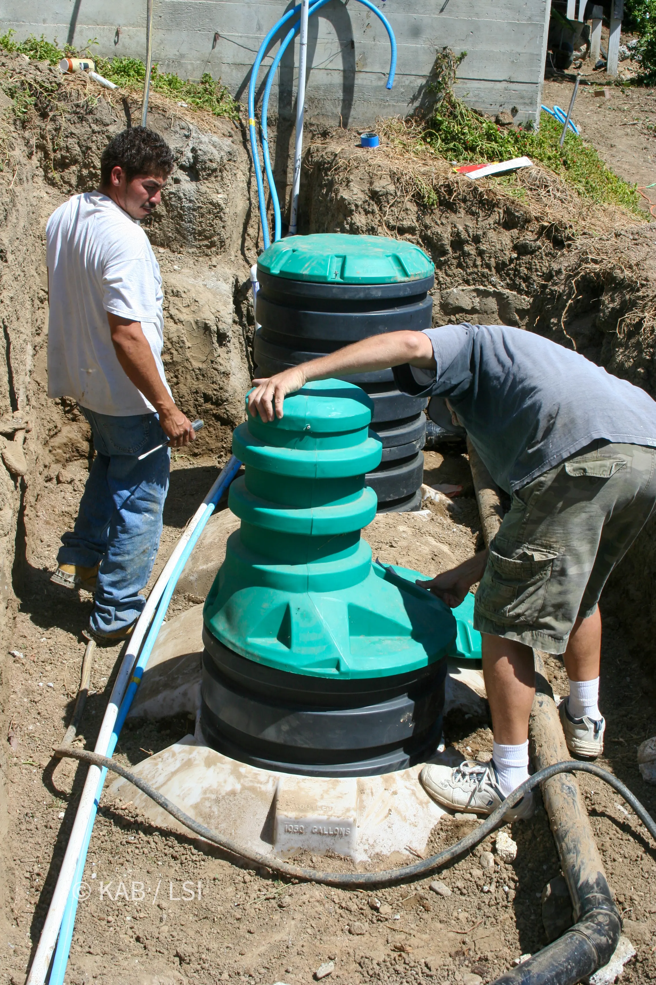 Worker assembling stacked riser sections onto the access opening of a new polyethylene septic tank