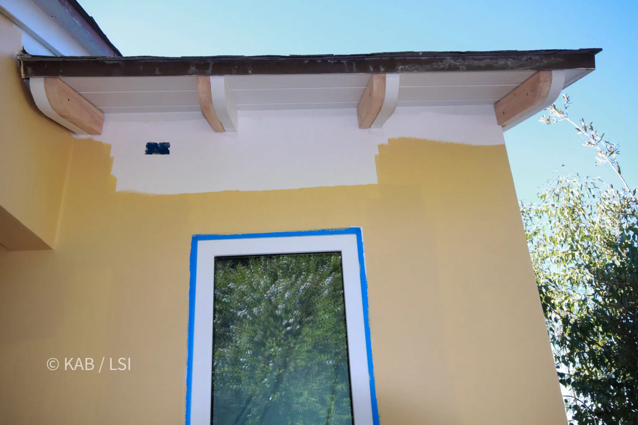 Freshly primed rafter tails, corbels and fascia above a partially repainted stucco wall