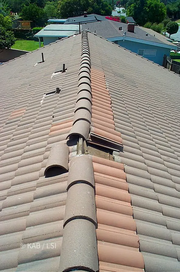 Mismatched replacement concrete roof tiles and loose ridge caps from a previous failed roof repair