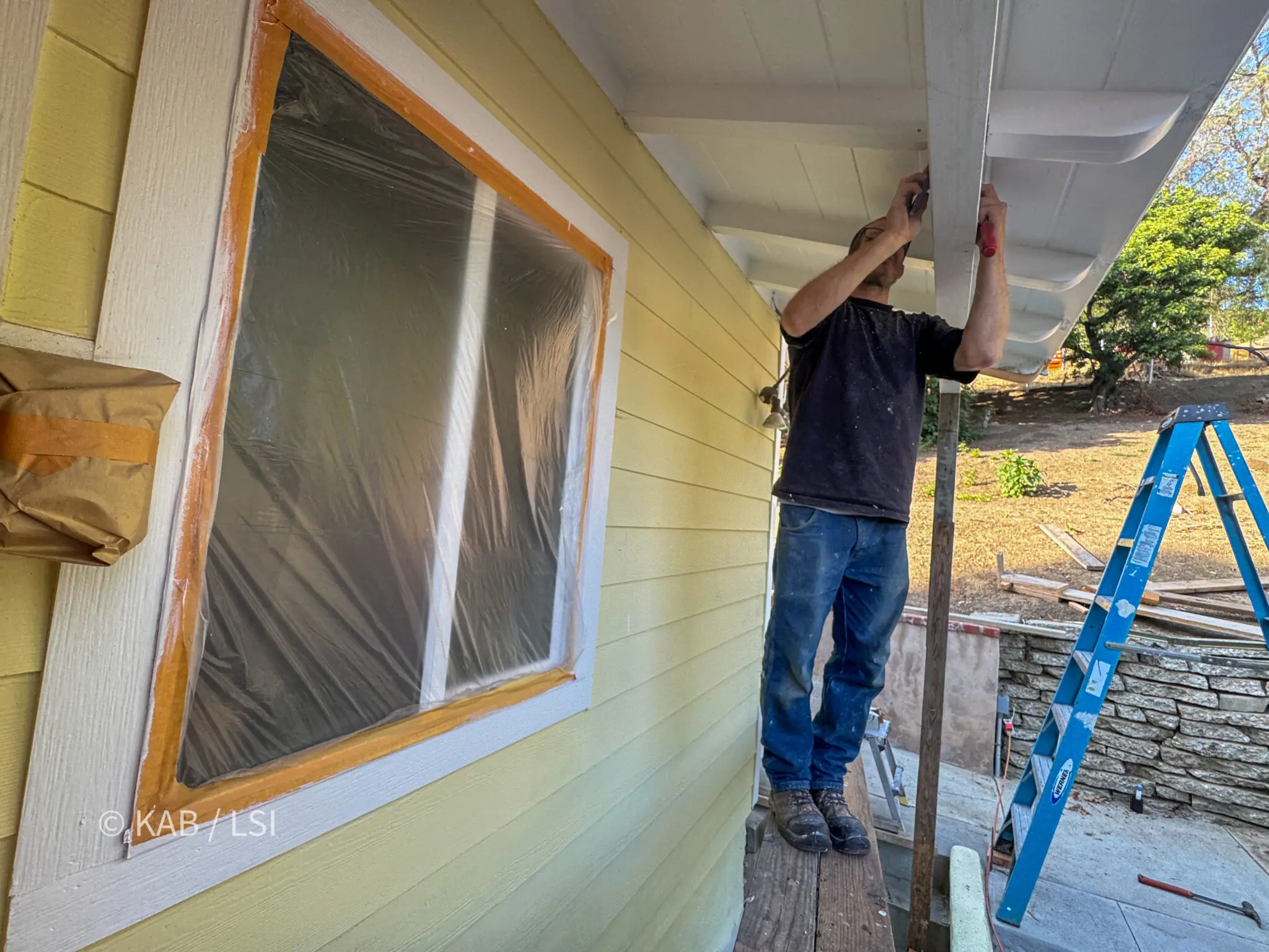 Handyman completing finish carpentry and painting beneath a repaired roof overhang