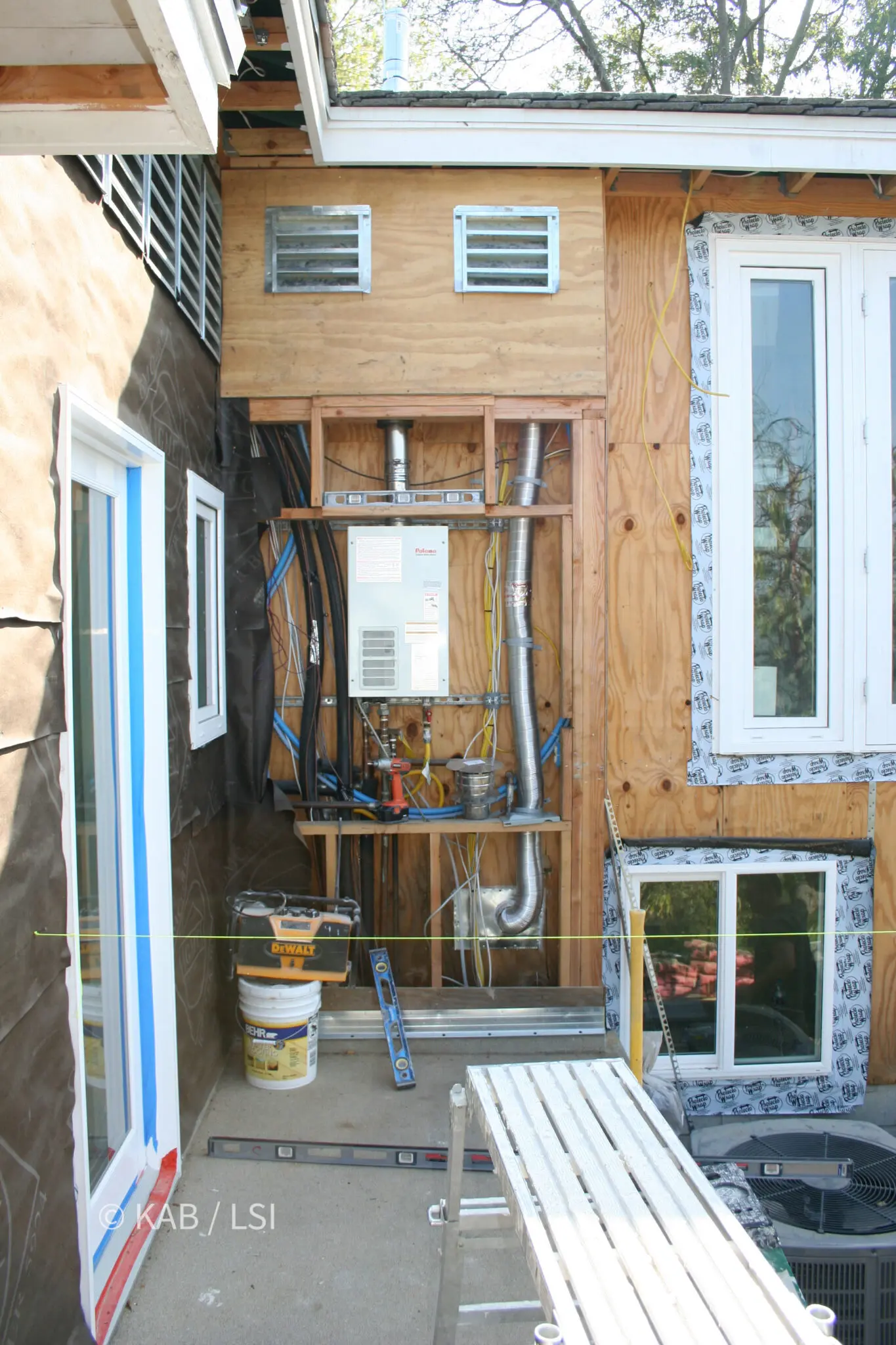 Tankless water heater alongside the electrical panel and service on open framing before the exterior wall is enclosed