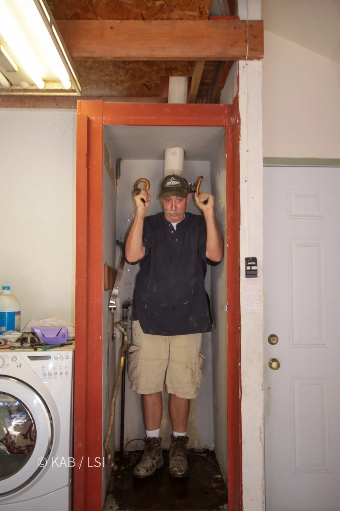 Man standing inside the full-height closet a forty-gallon tank water heater used to occupy, beside the laundry