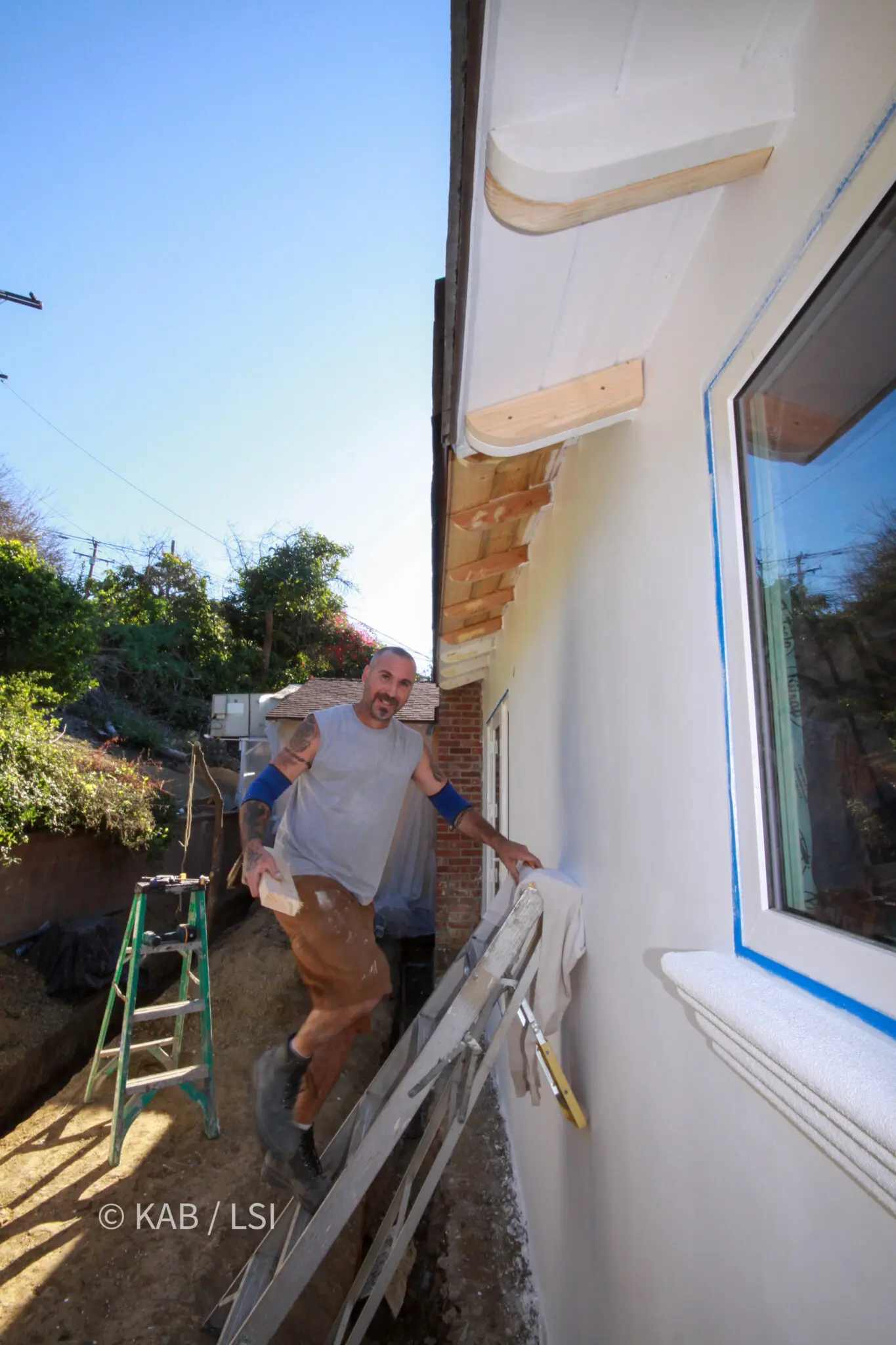 Painter on an extension ladder finishing the columns and eave of a rebuilt second-story loggia