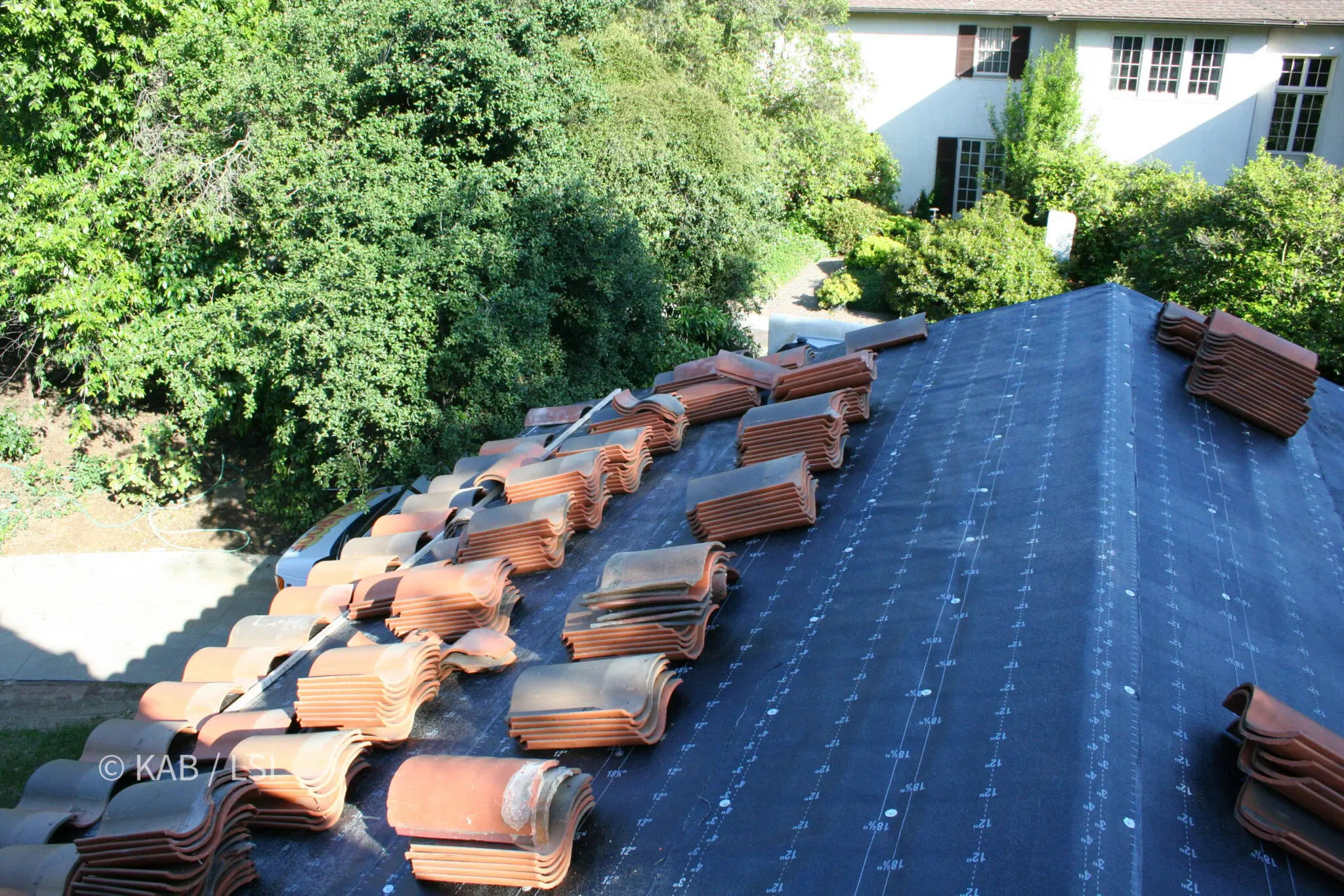 Historic clay roof tile staged across a re-papered roof deck before reinstallation on a 1920s carriage house