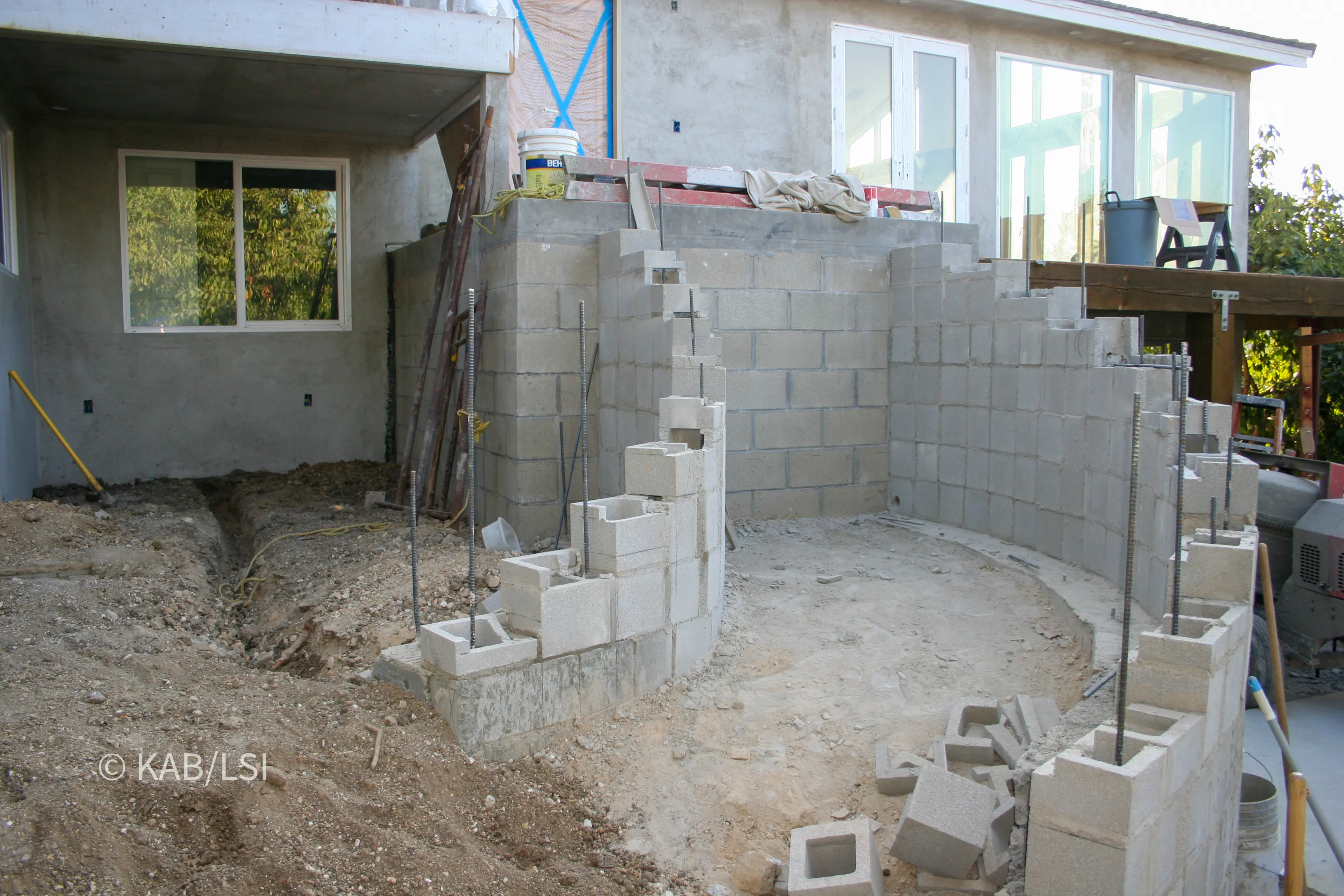 Concrete block walls being laid in an excavated pit alongside a hillside house to form a below-grade safe room and valuable storage vault