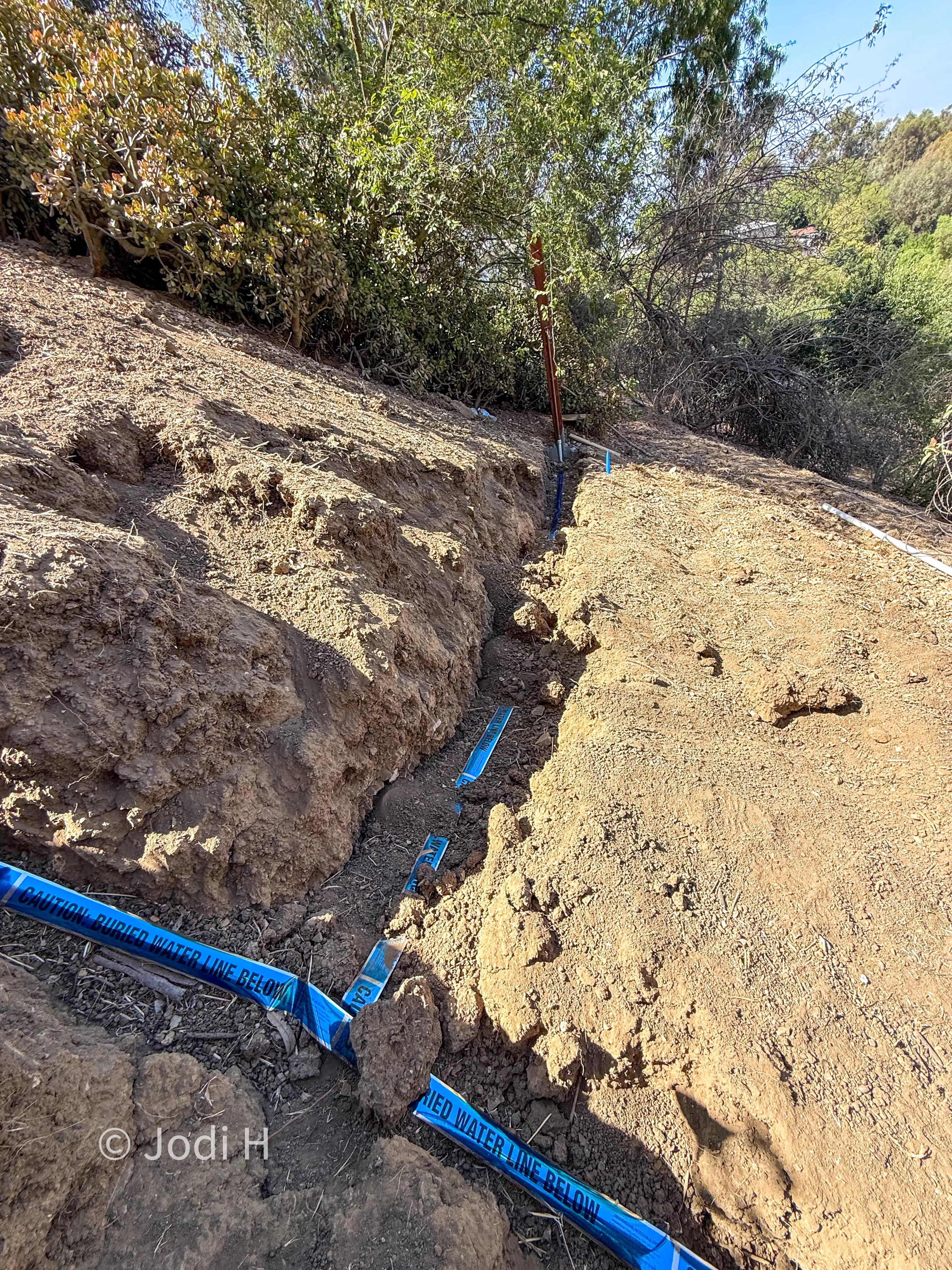 Water service trench cut through rock and hard fill on a hillside