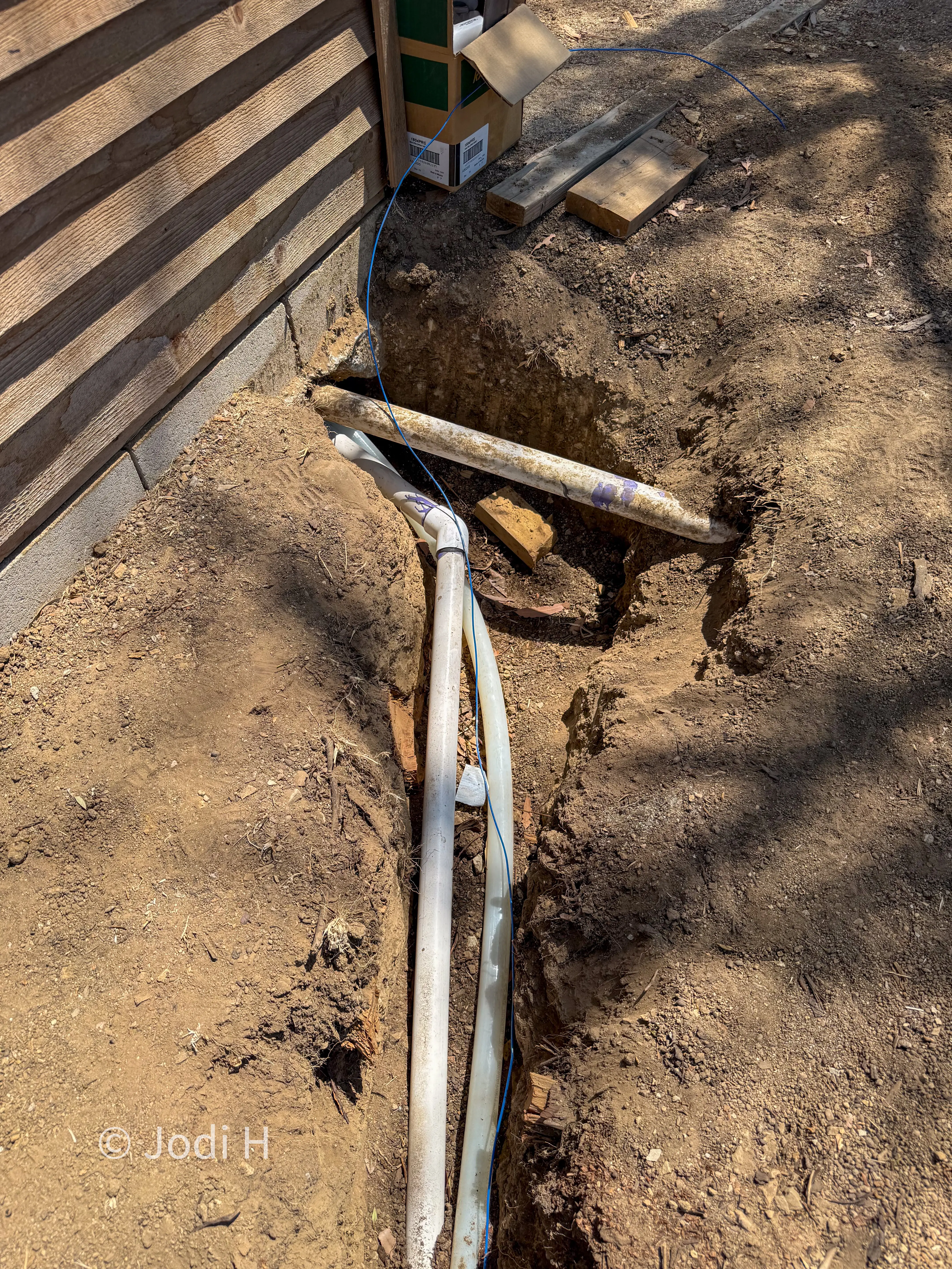 Two parallel water service lines entering an open trench beside a wooden deck on a hillside property in La Habra Heights