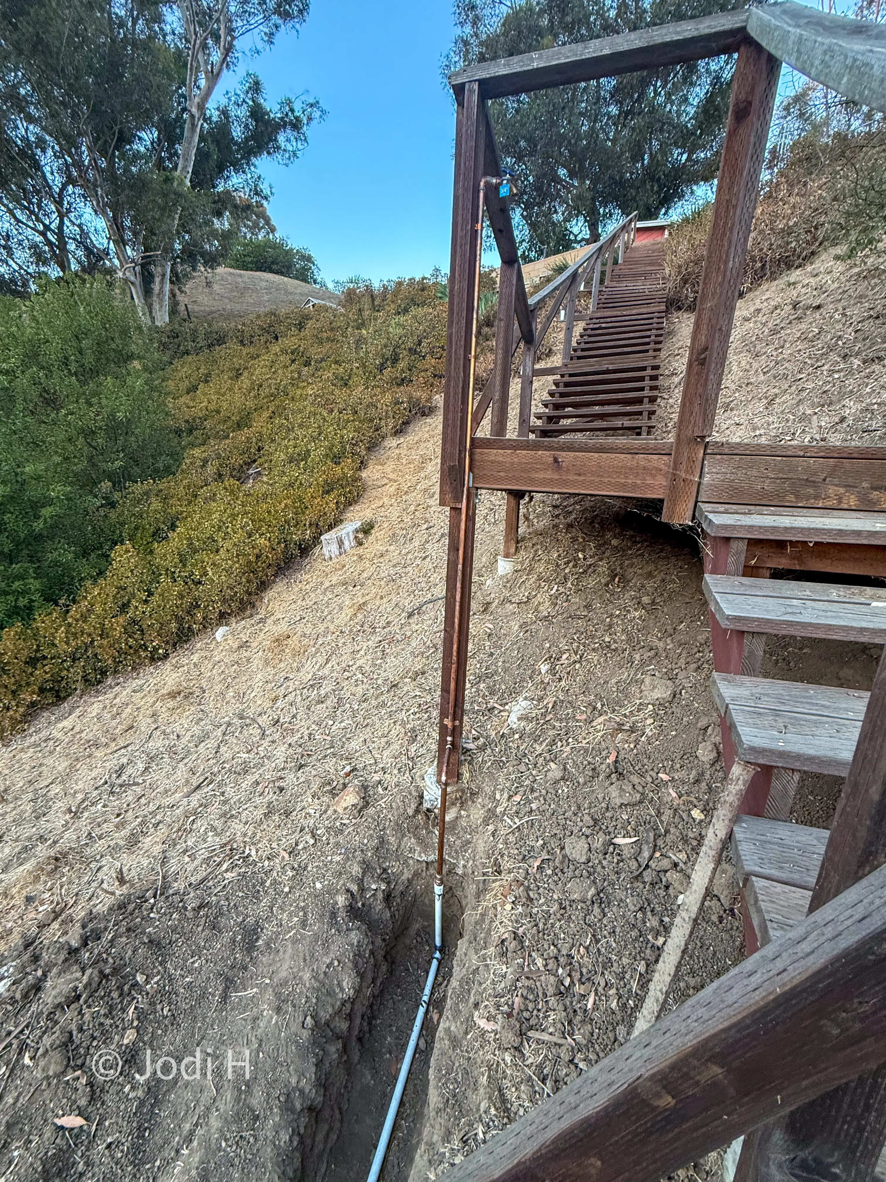 Long wooden staircase descending a brush-covered hillside slope on a hillside property in La Habra Heights