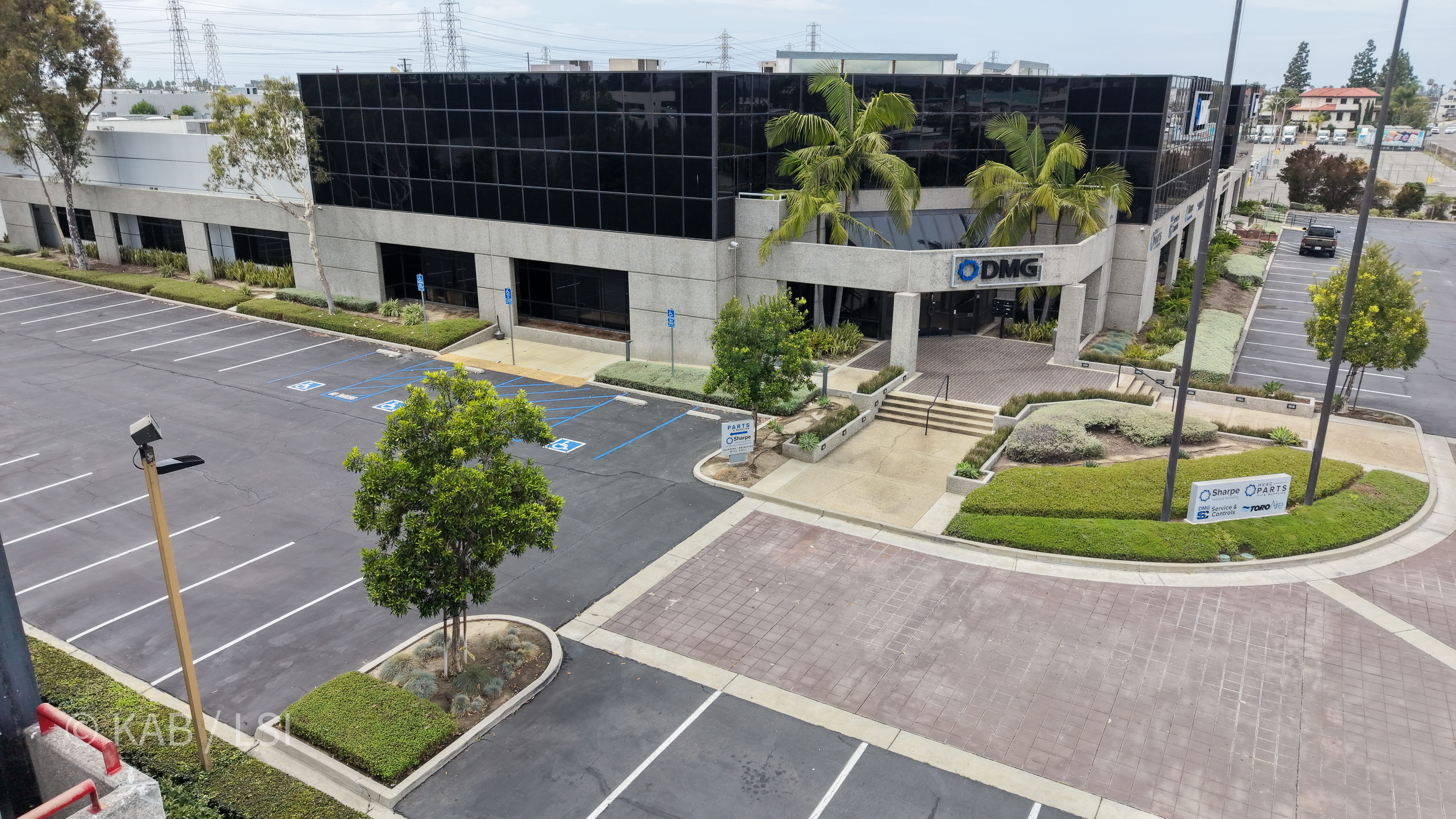 Front entry of the 88,000 sq ft commercial building at 1110 W. Taft Ave., Orange, CA, with DMG HVAC signage above the portico, queen palms, brick paver walkway, and tenant directory monument visible.